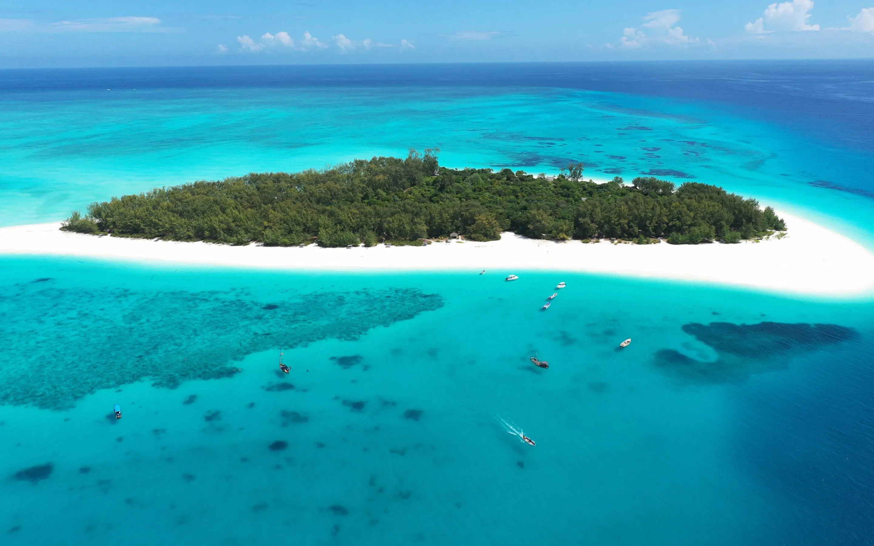 Mnemba Island sits within bright turquoise water, with white sand, coral patches, and boats offshore in Tanzania.