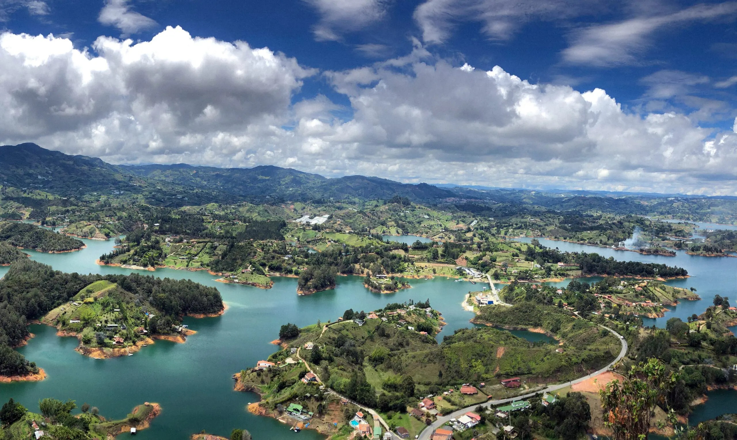 An aerial view looks over a green lake, forested slopes, and winding roads on a drive outside Medellín, Colombia.