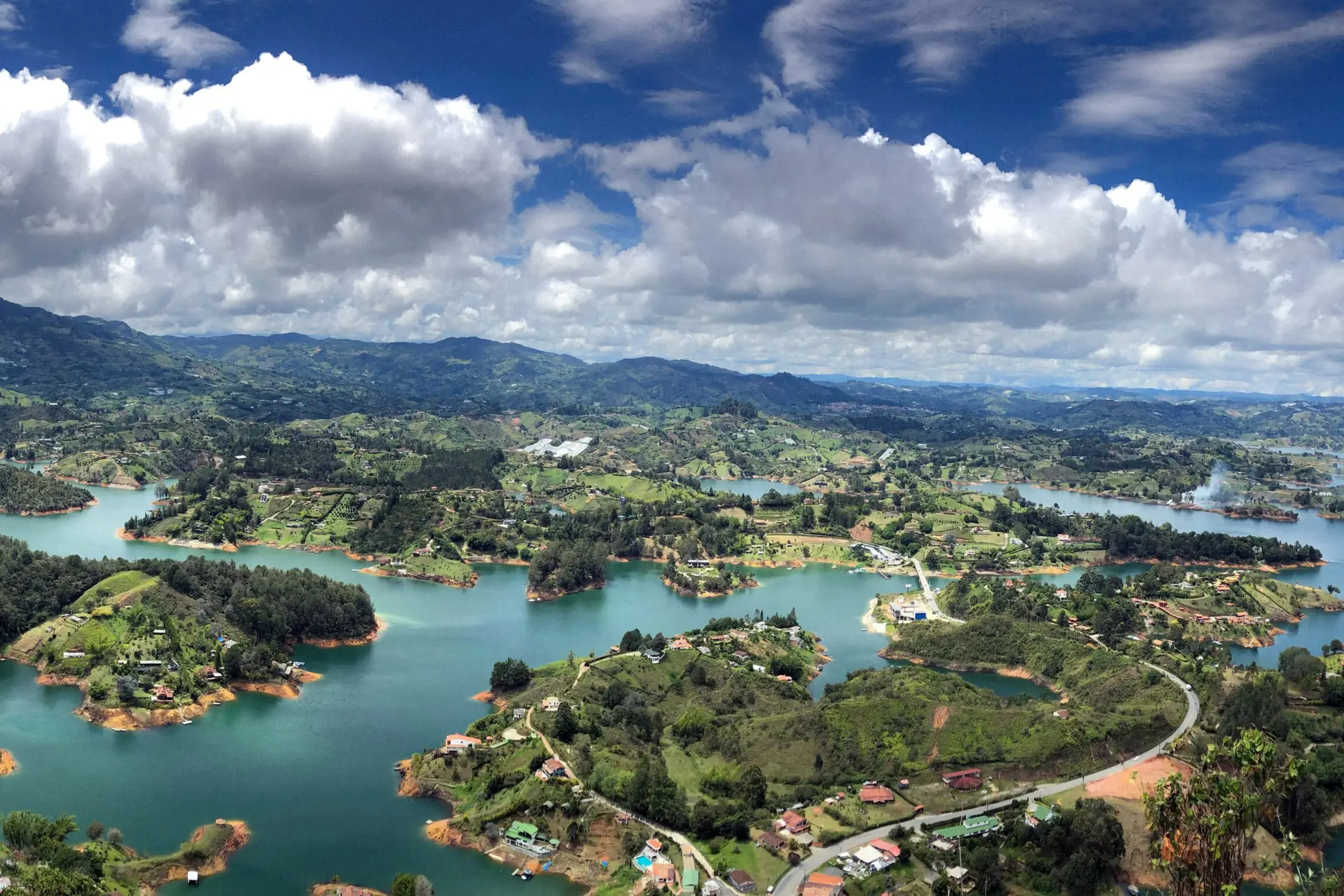 An aerial view looks over a green lake, forested slopes, and winding roads on a drive outside Medellín, Colombia.