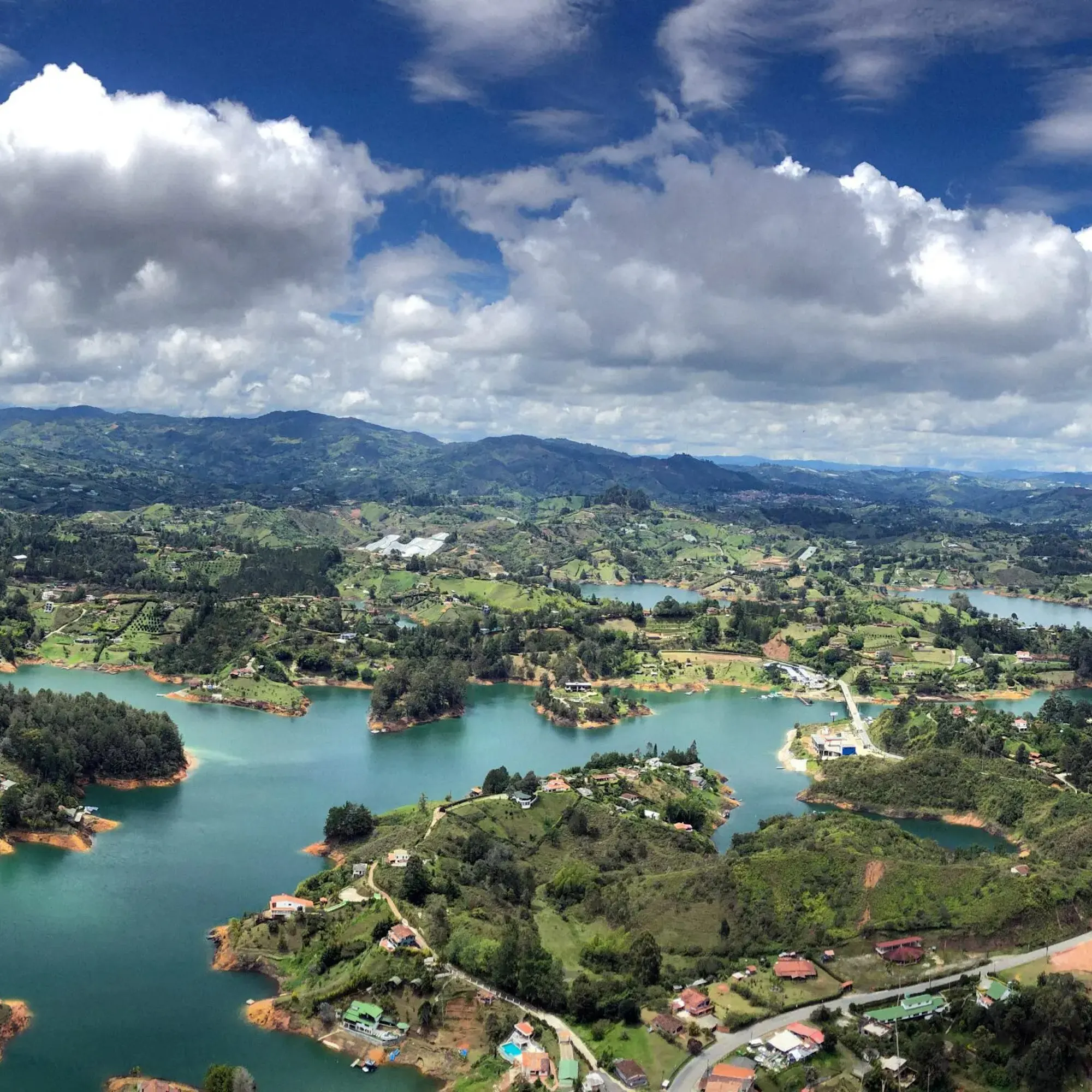 An aerial view looks over a green lake, forested slopes, and winding roads on a drive outside Medellín, Colombia.