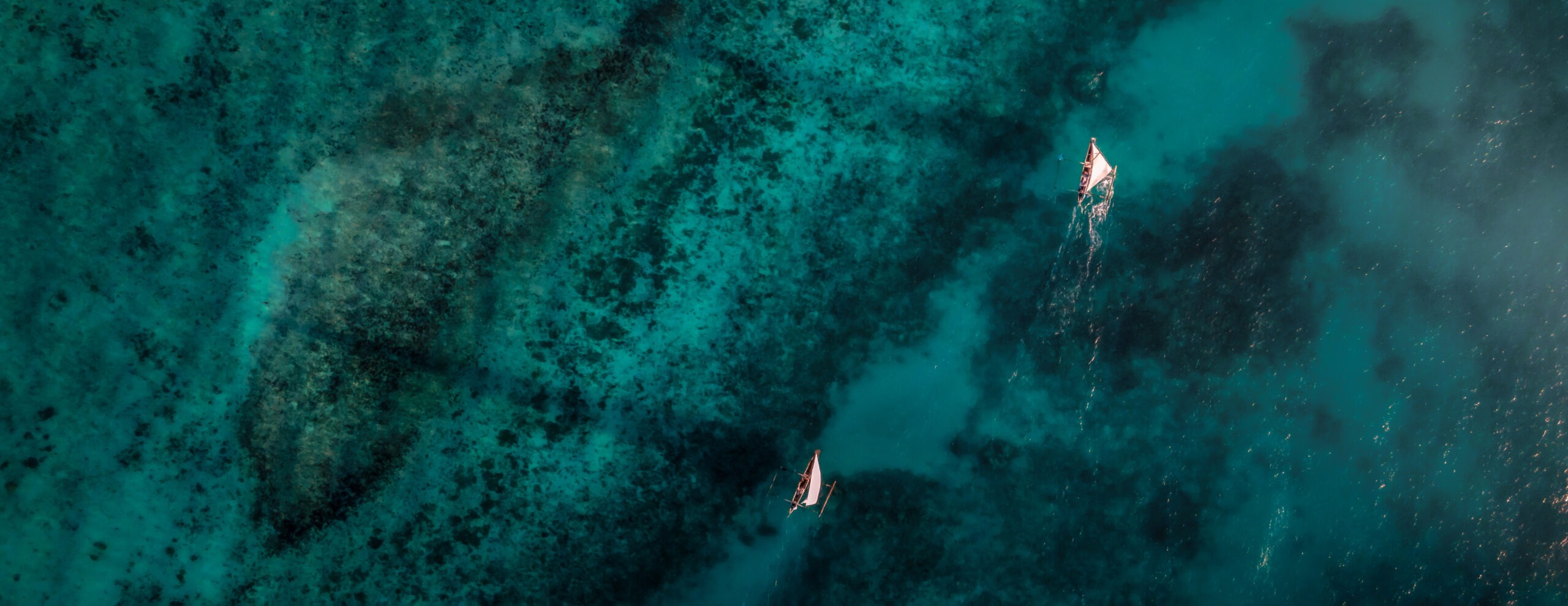Aerial water shows boats drifting over dark coral reefs and turquoise channels off Pemba Island in Tanzania.