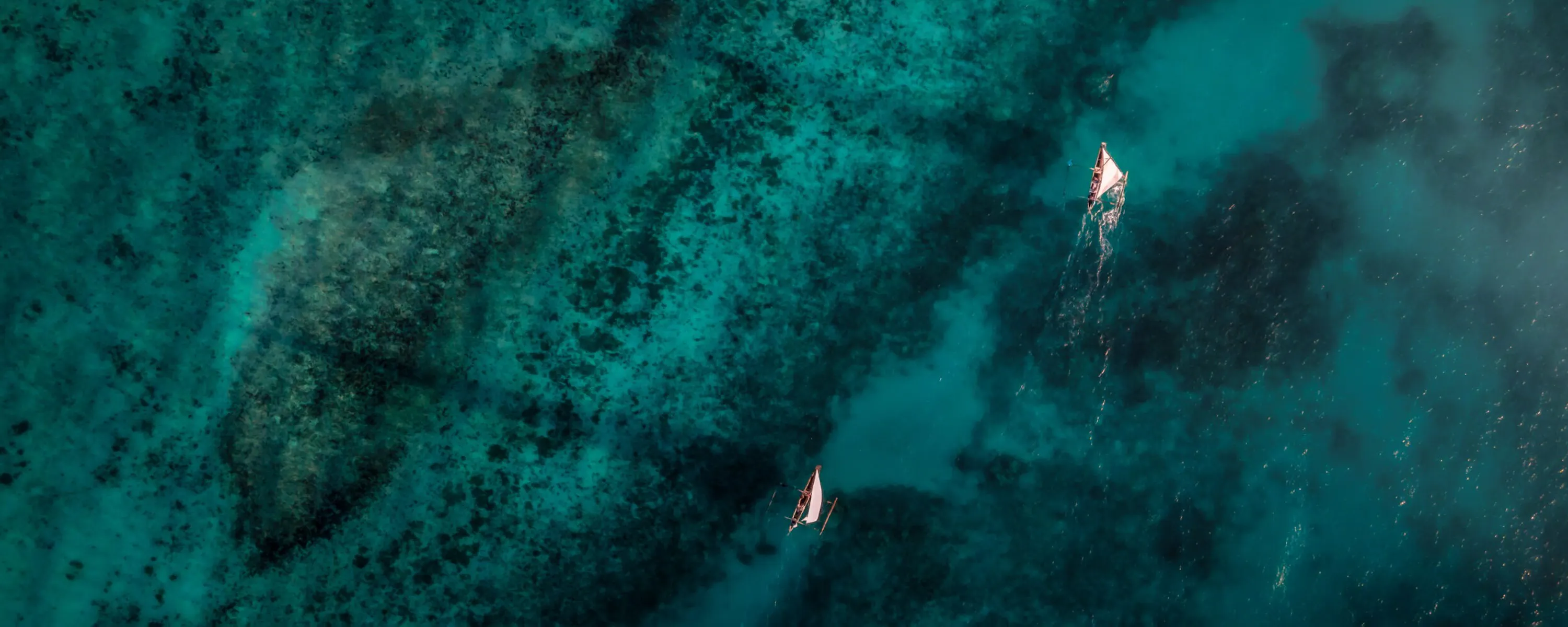Aerial water shows boats drifting over dark coral reefs and turquoise channels off Pemba Island in Tanzania.