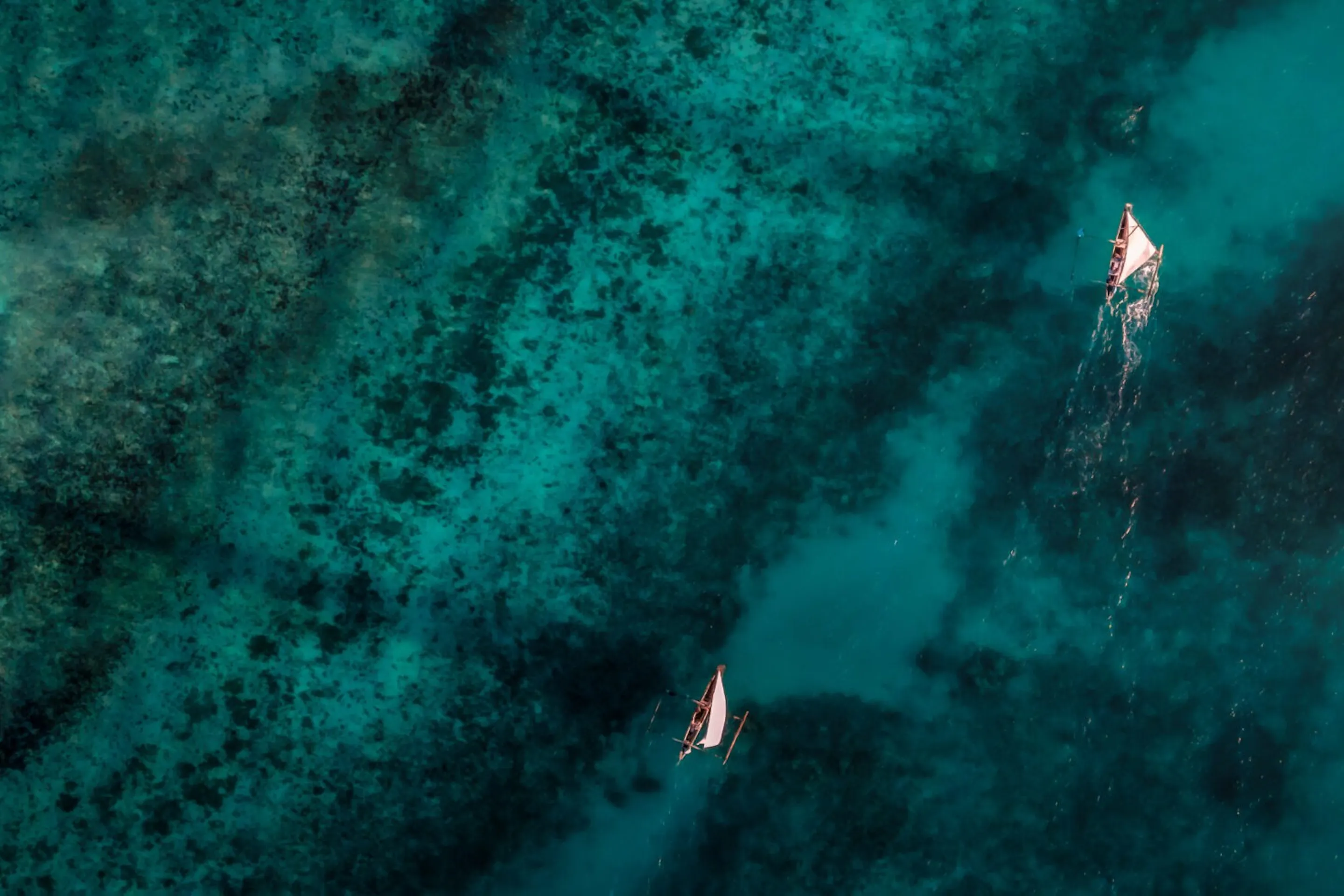 Aerial water shows boats drifting over dark coral reefs and turquoise channels off Pemba Island in Tanzania.