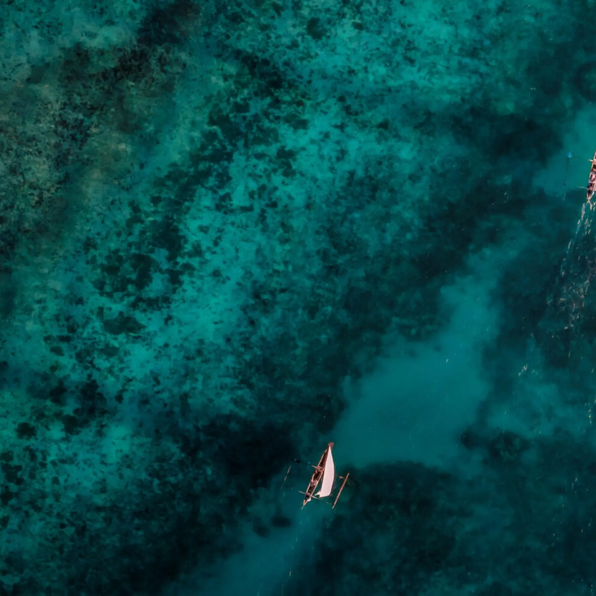 Aerial water shows boats drifting over dark coral reefs and turquoise channels off Pemba Island in Tanzania.
