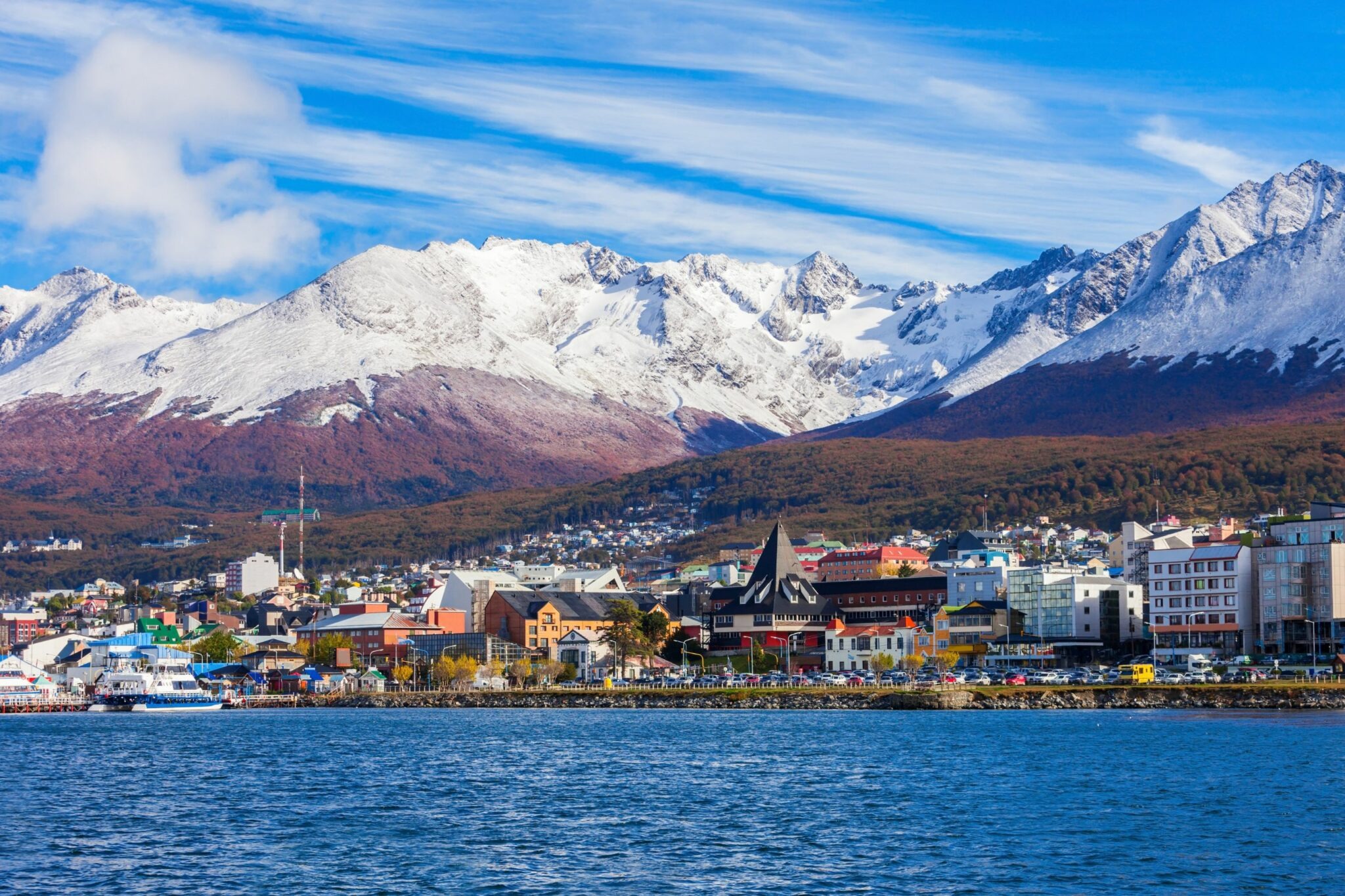 Ushuaia's waterfront stretches below snowy mountains, with colorful buildings lining the shore in Patagonia.