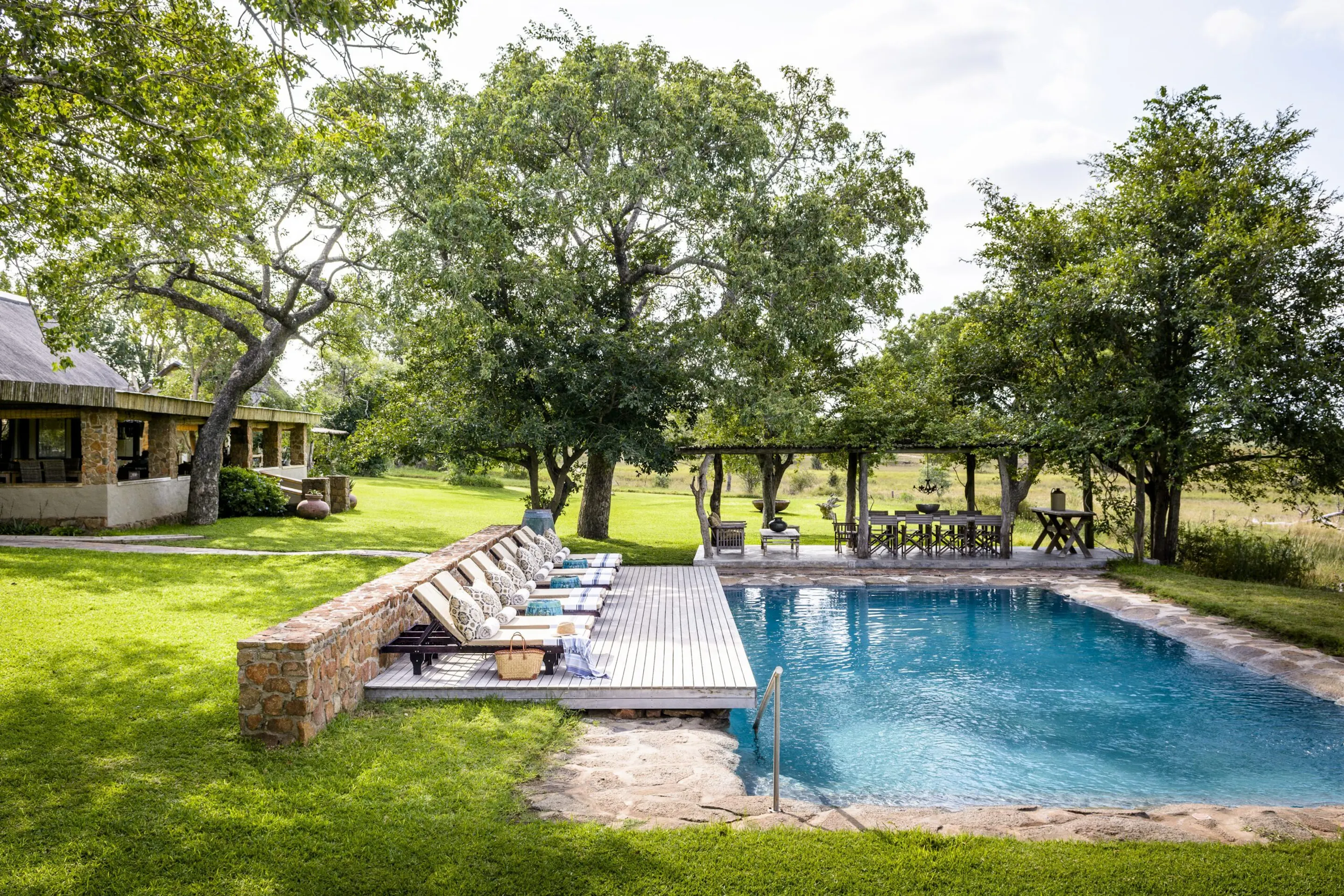 A swimming pool and loungers sit beside lawns, shaded paths, and leafy trees at Singita Castleton in South Africa.