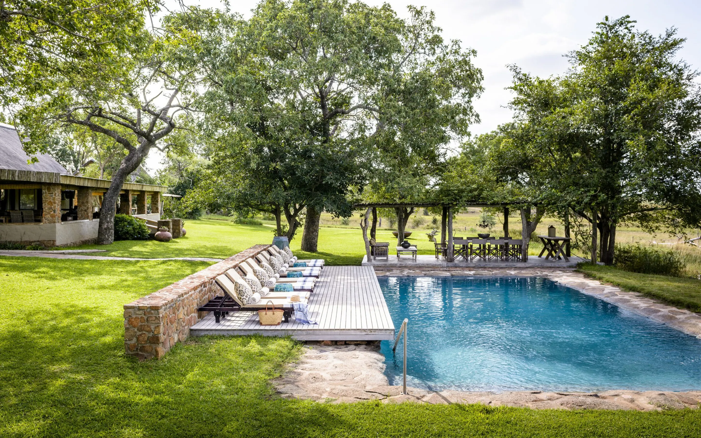 A swimming pool and loungers sit beside lawns, shaded paths, and leafy trees at Singita Castleton in South Africa.