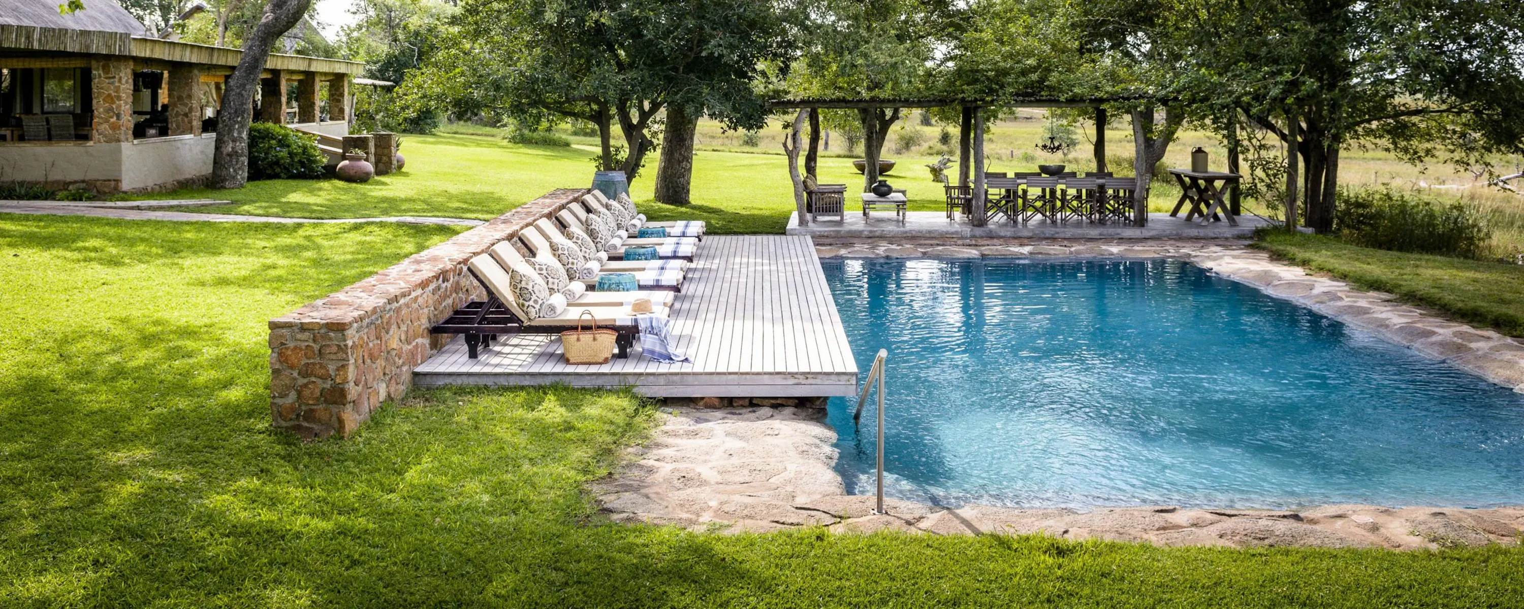 A swimming pool and loungers sit beside lawns, shaded paths, and leafy trees at Singita Castleton in South Africa.
