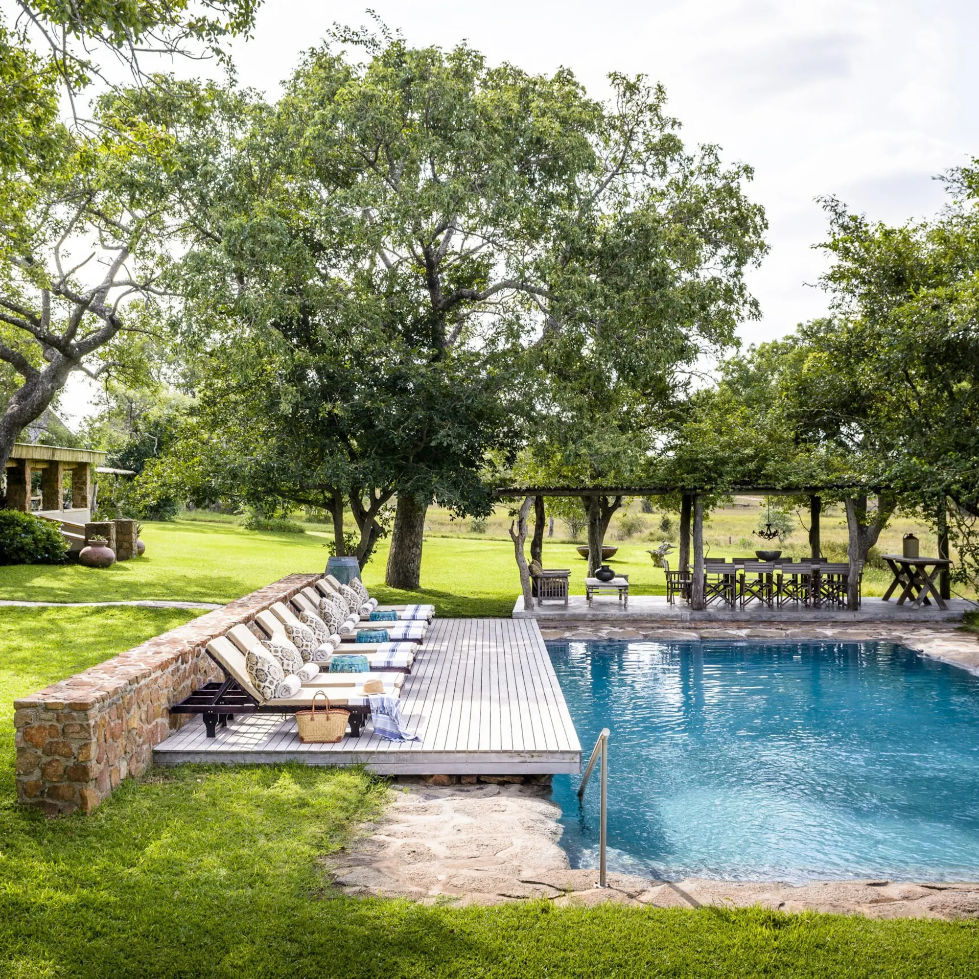 A swimming pool and loungers sit beside lawns, shaded paths, and leafy trees at Singita Castleton in South Africa.