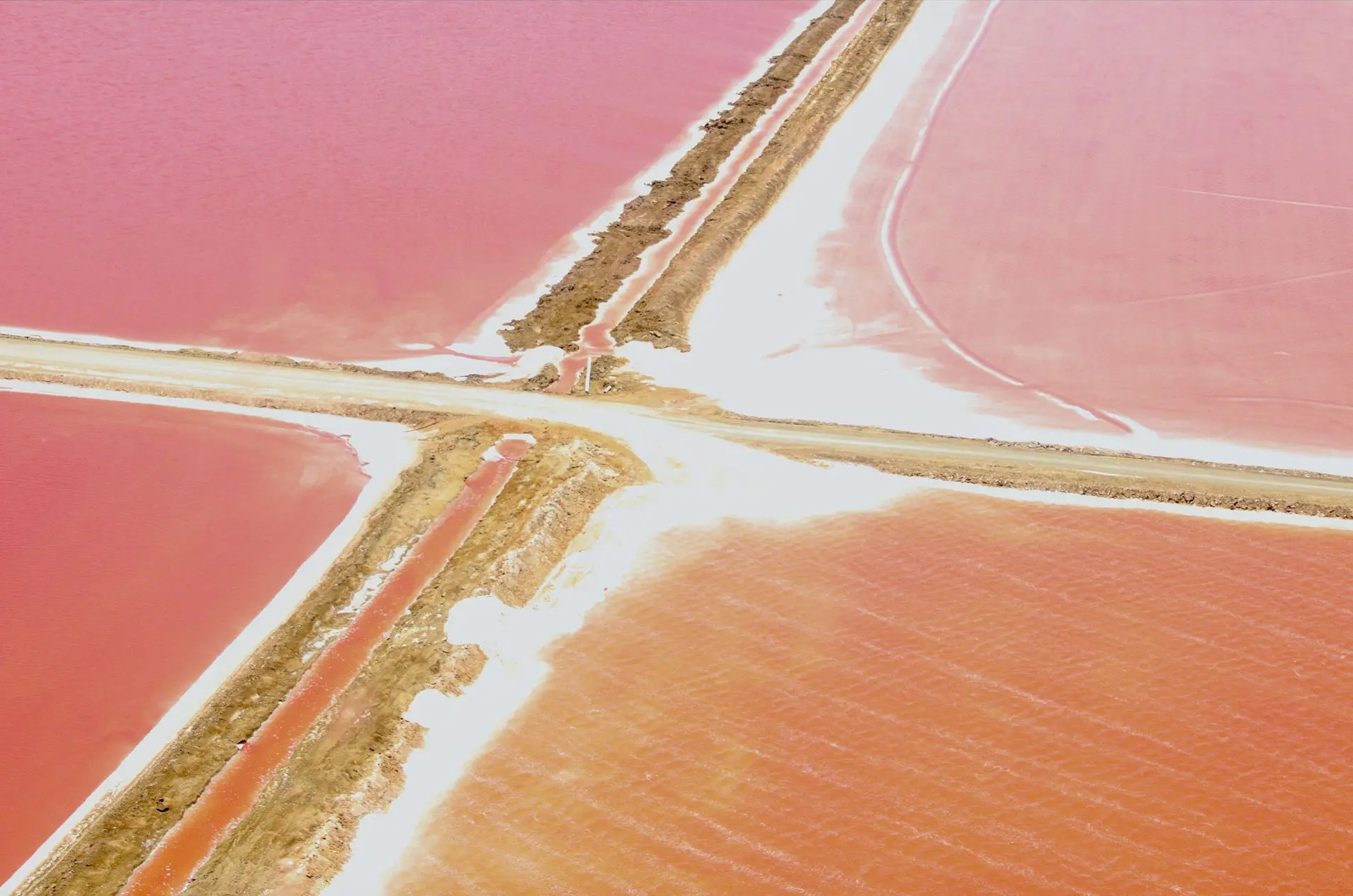 An aerial view shows pink salt pans divided by pale roads and embankments along Namibia's Atlantic coast.