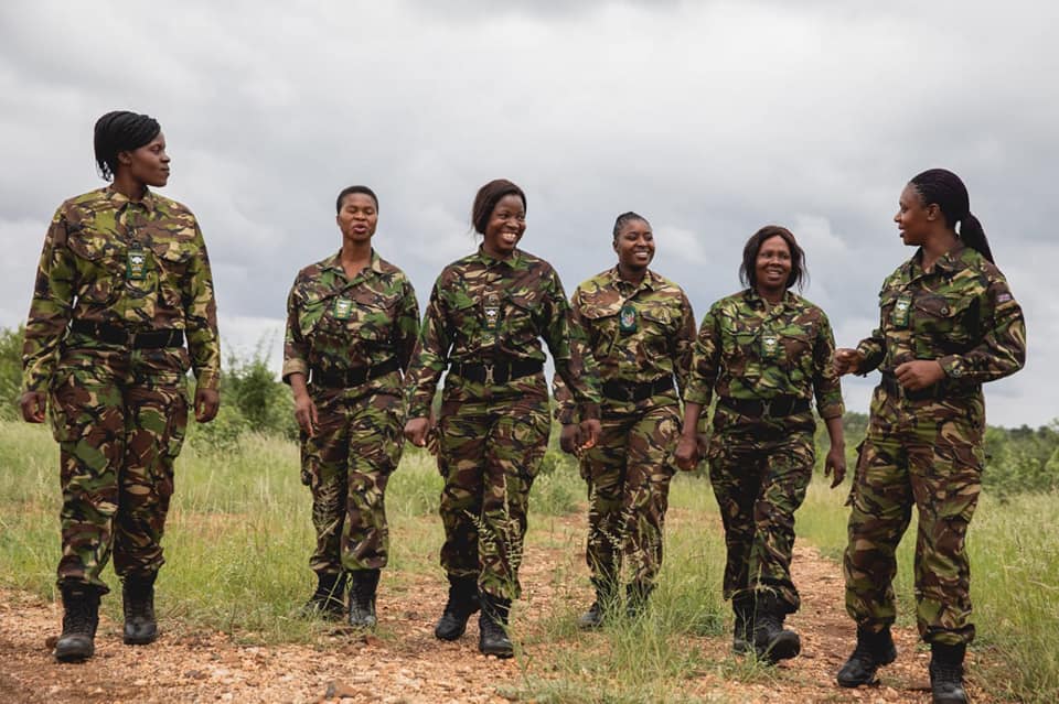 A group of 6 women, part of South Africa's Black Mambas, the first all-female anti-poaching unit, stand in a row in uniform.