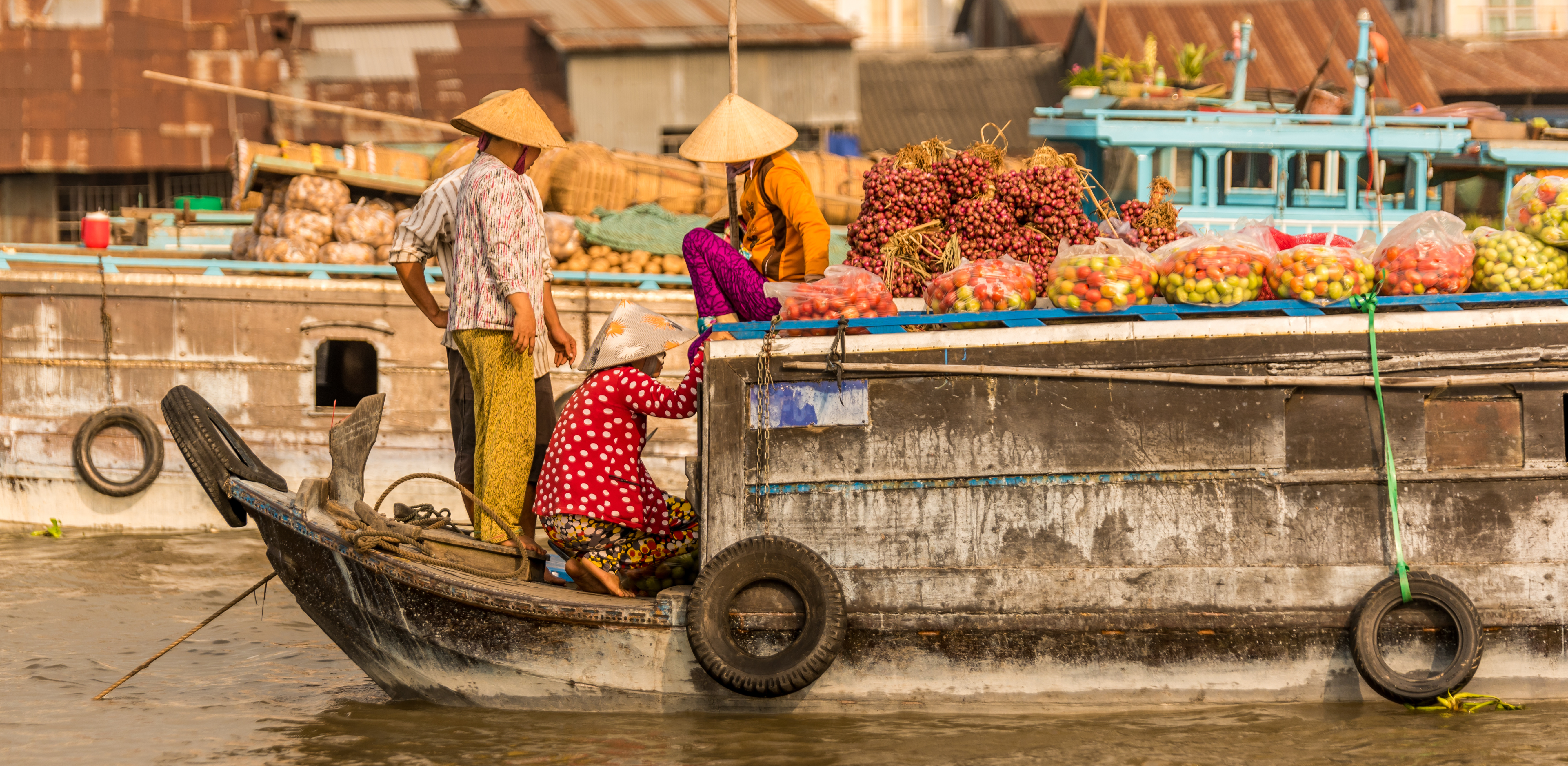 A vendor in a conical hat paddles a wooden boat through a floating market on the Mekong Delta.