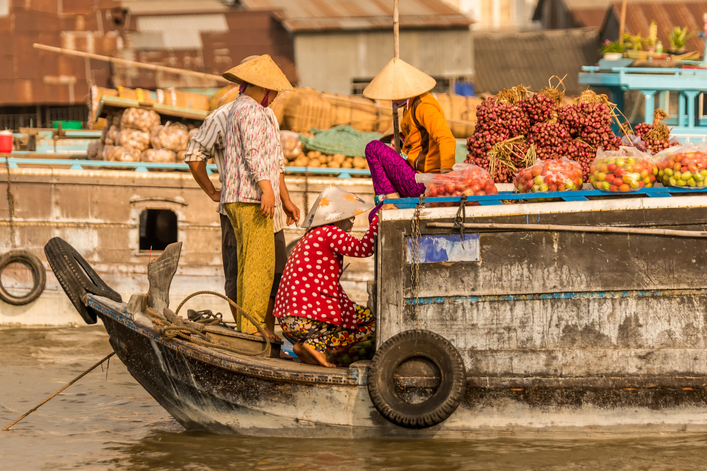 A vendor in a conical hat paddles a wooden boat through a floating market on the Mekong Delta.