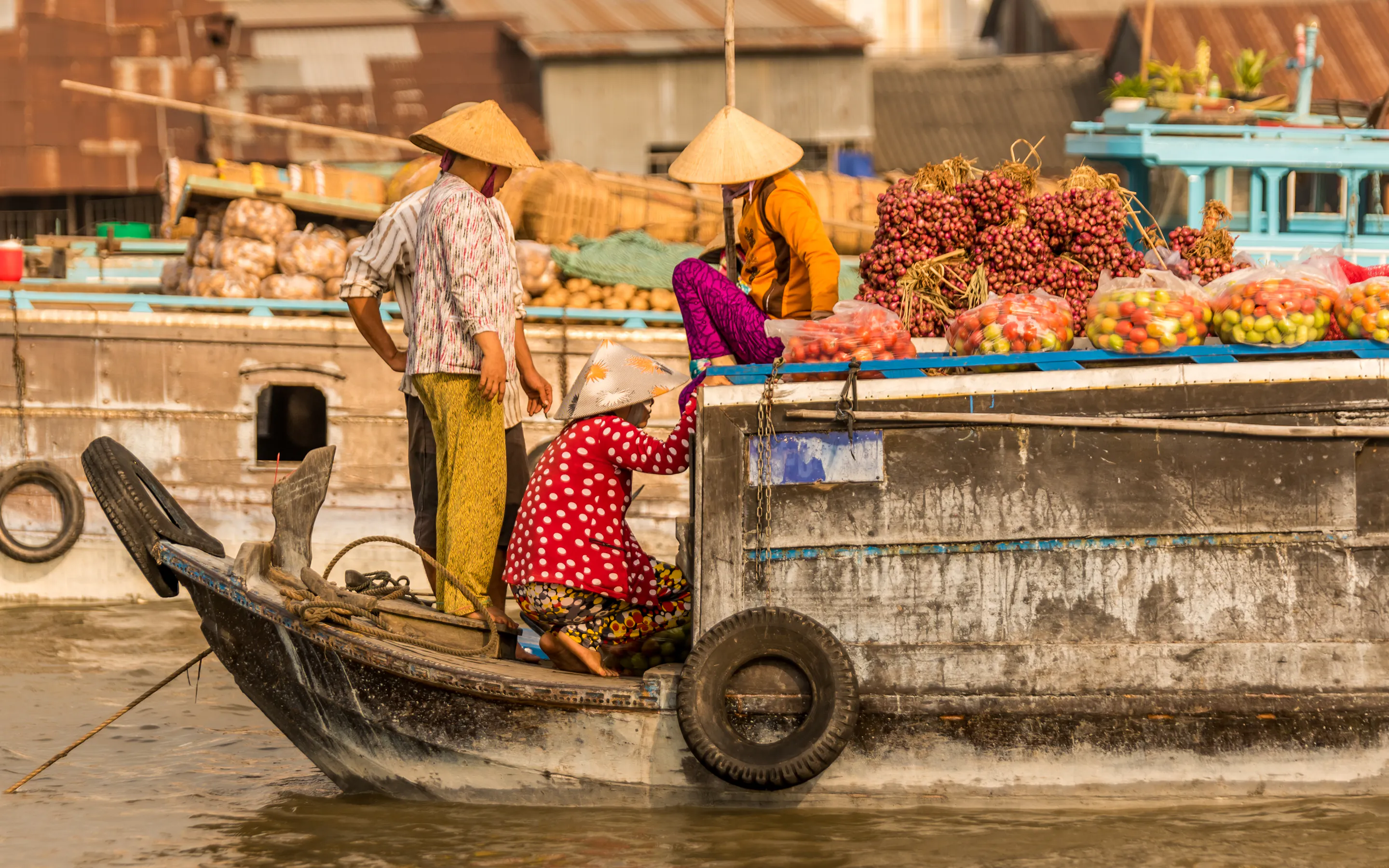 A vendor in a conical hat paddles a wooden boat through a floating market on the Mekong Delta.