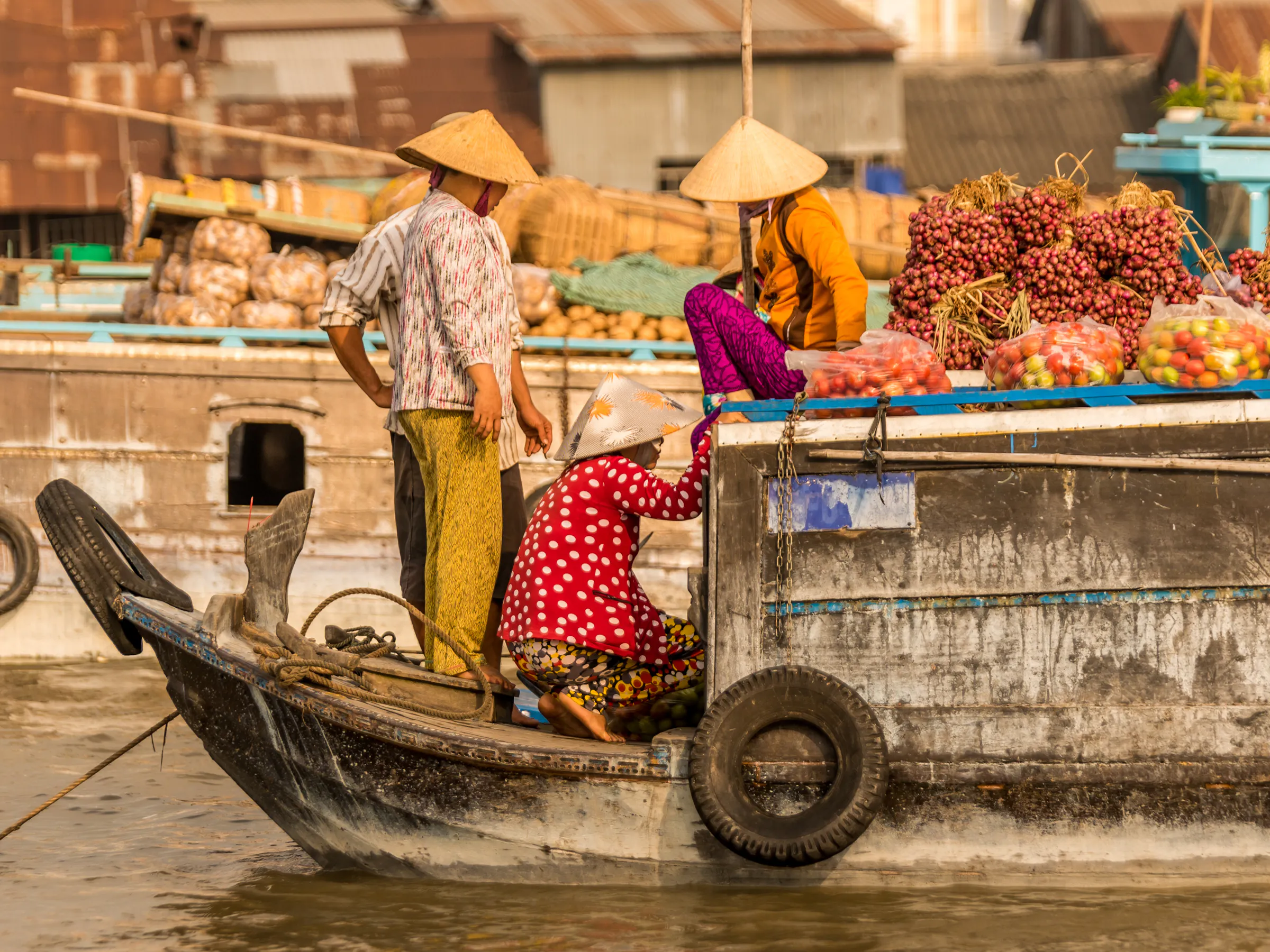 A vendor in a conical hat paddles a wooden boat through a floating market on the Mekong Delta.