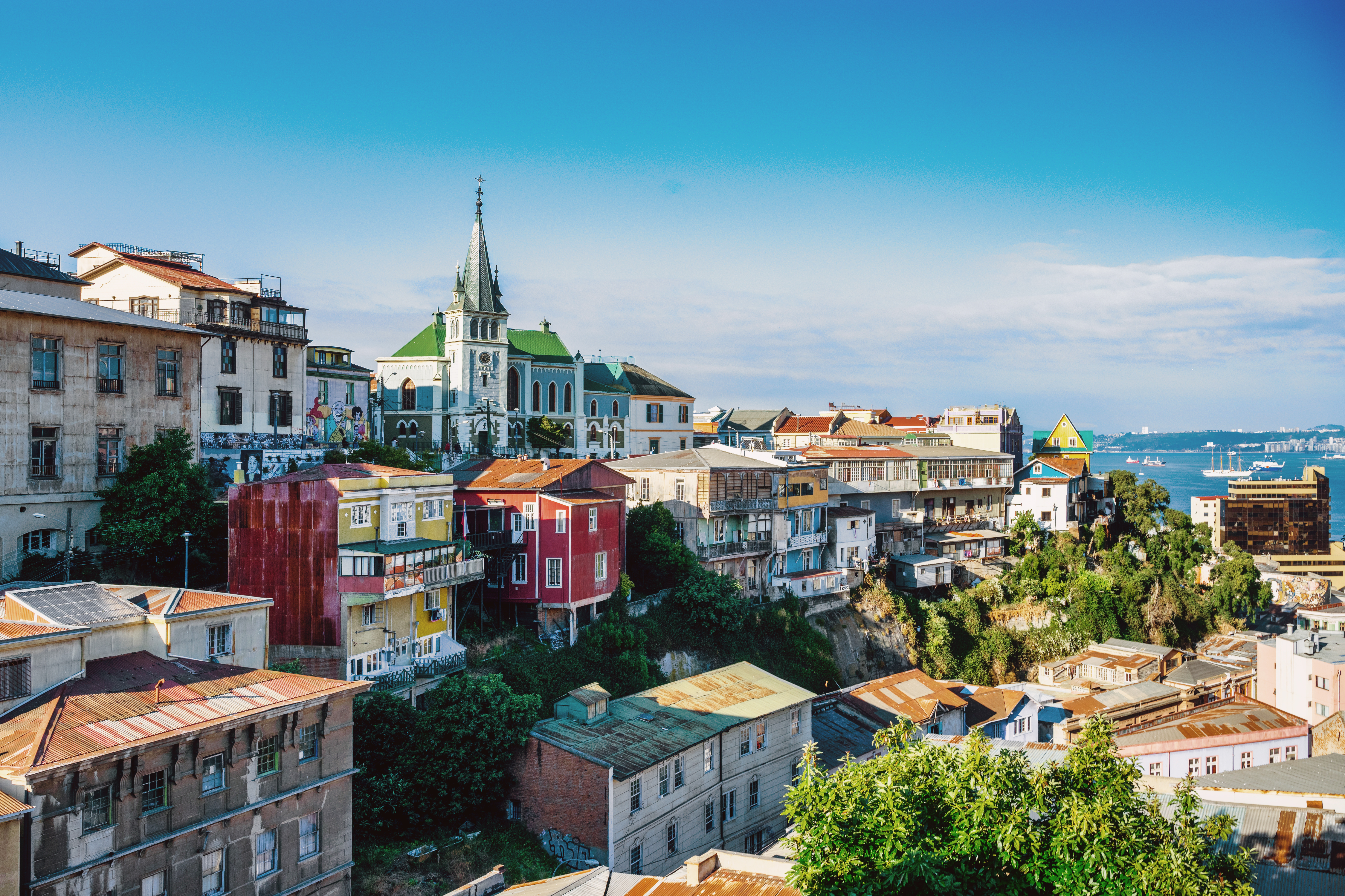 Colorful hillside neighborhoods of Valparaíso cascade down to the bay under a partly cloudy sky.