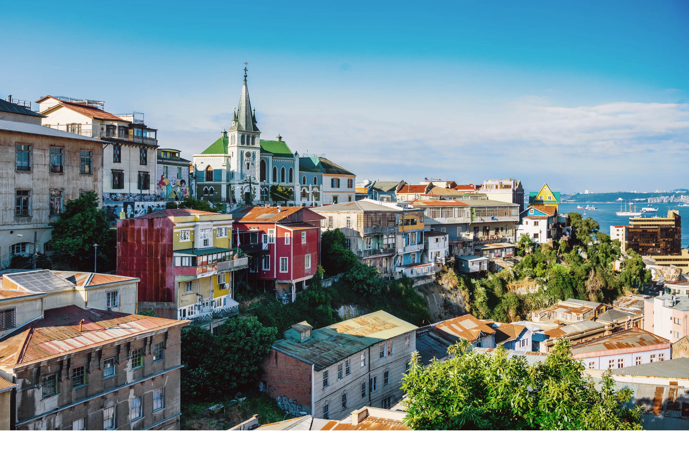 Colorful hillside neighborhoods of Valparaíso cascade down to the bay under a partly cloudy sky.