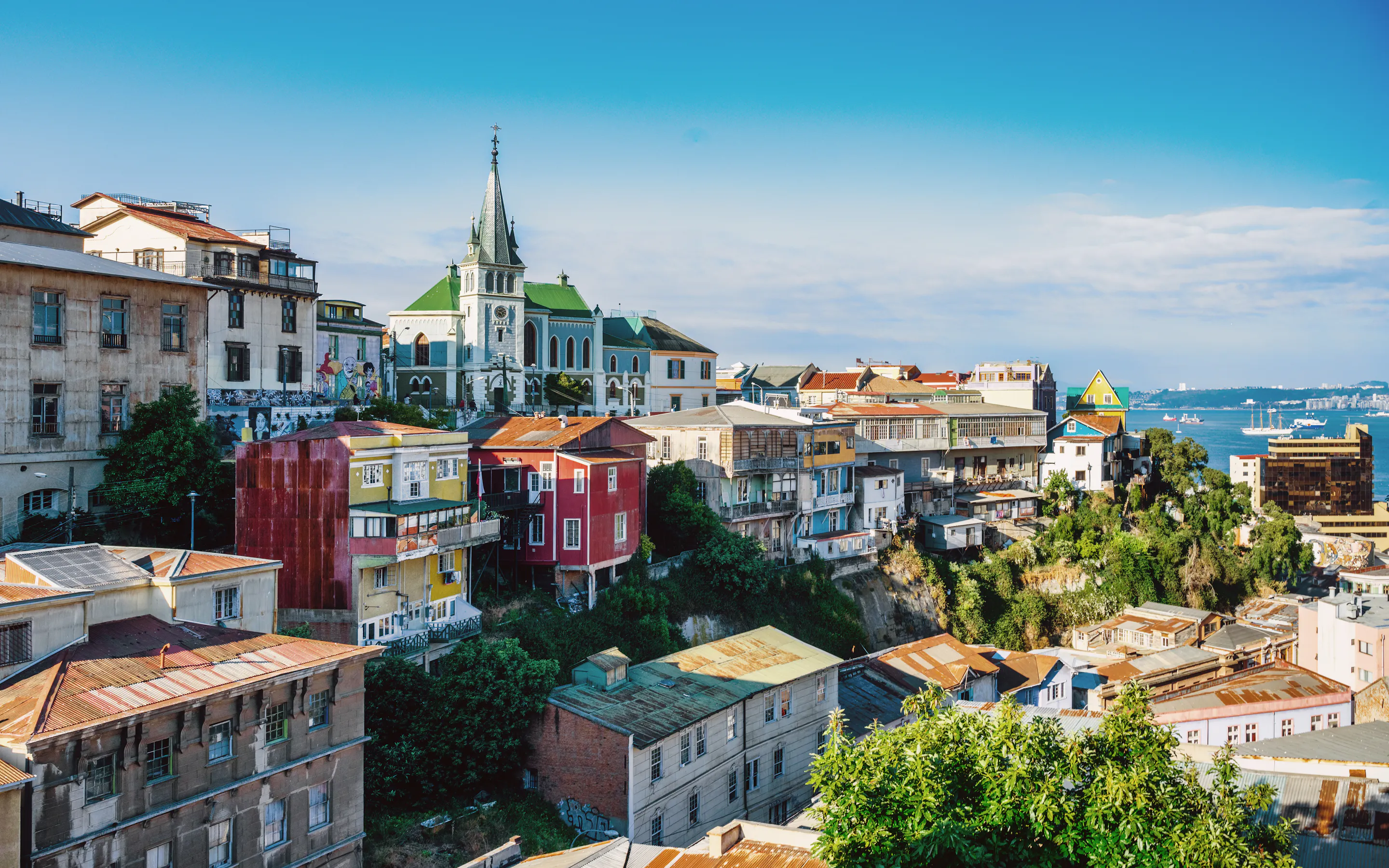 Colorful hillside neighborhoods of Valparaíso cascade down to the bay under a partly cloudy sky.