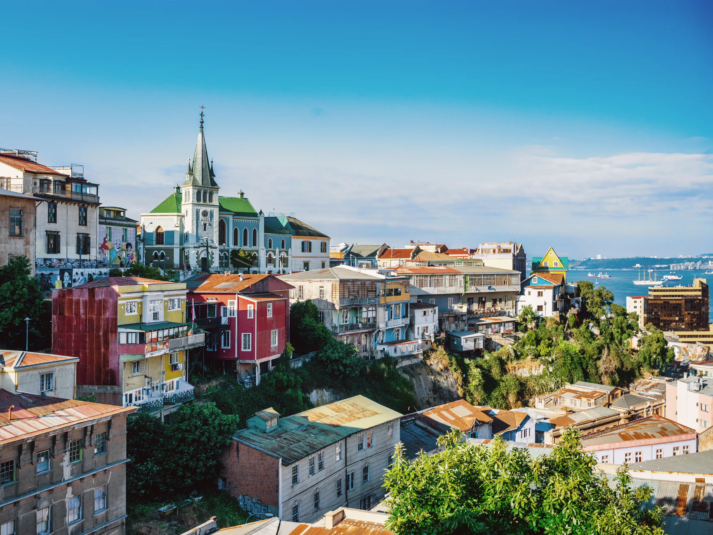 Colorful hillside neighborhoods of Valparaíso cascade down to the bay under a partly cloudy sky.