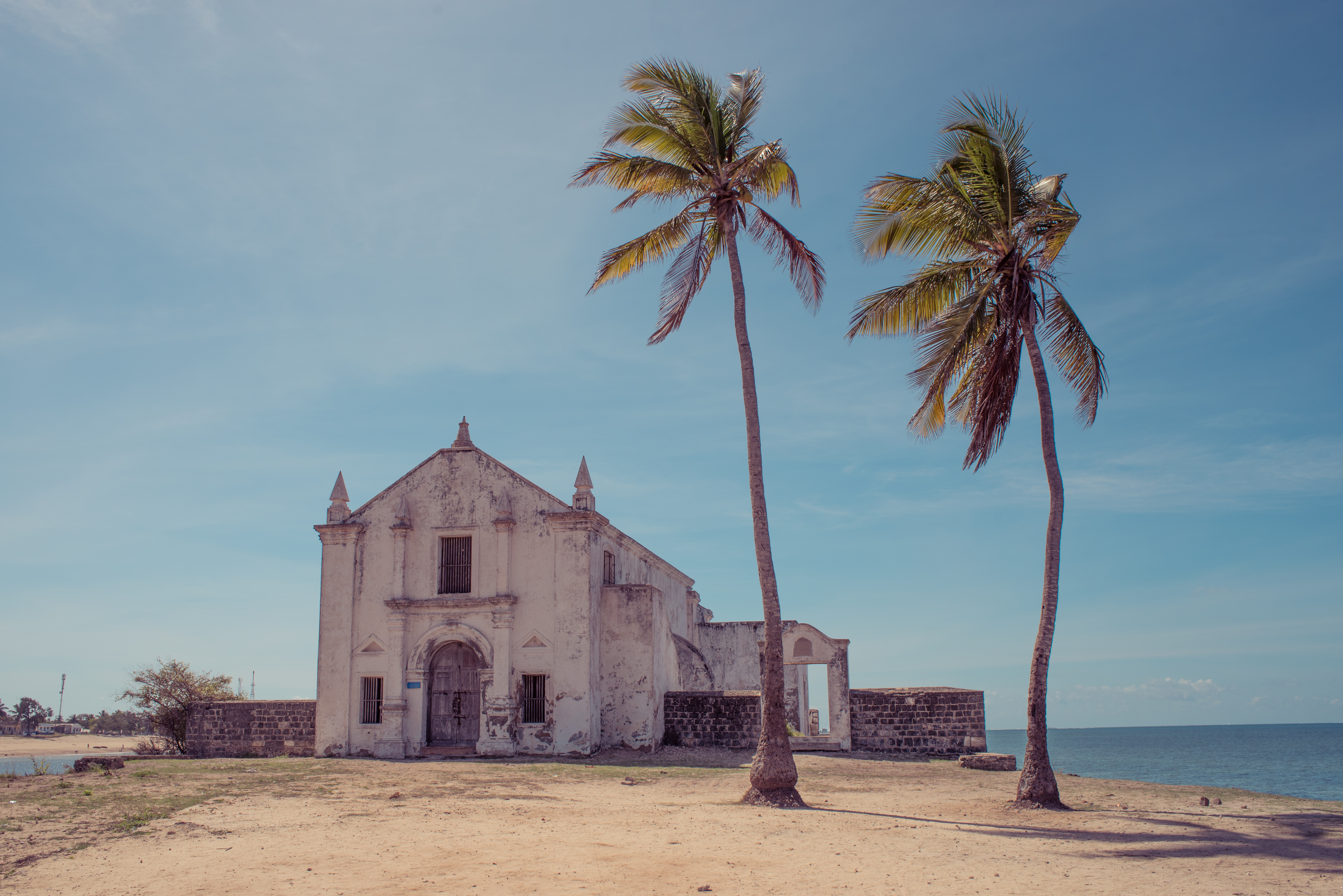 A whitewashed colonial church stands beside palm trees on the sandy shore of Ilha de Moçambique.
