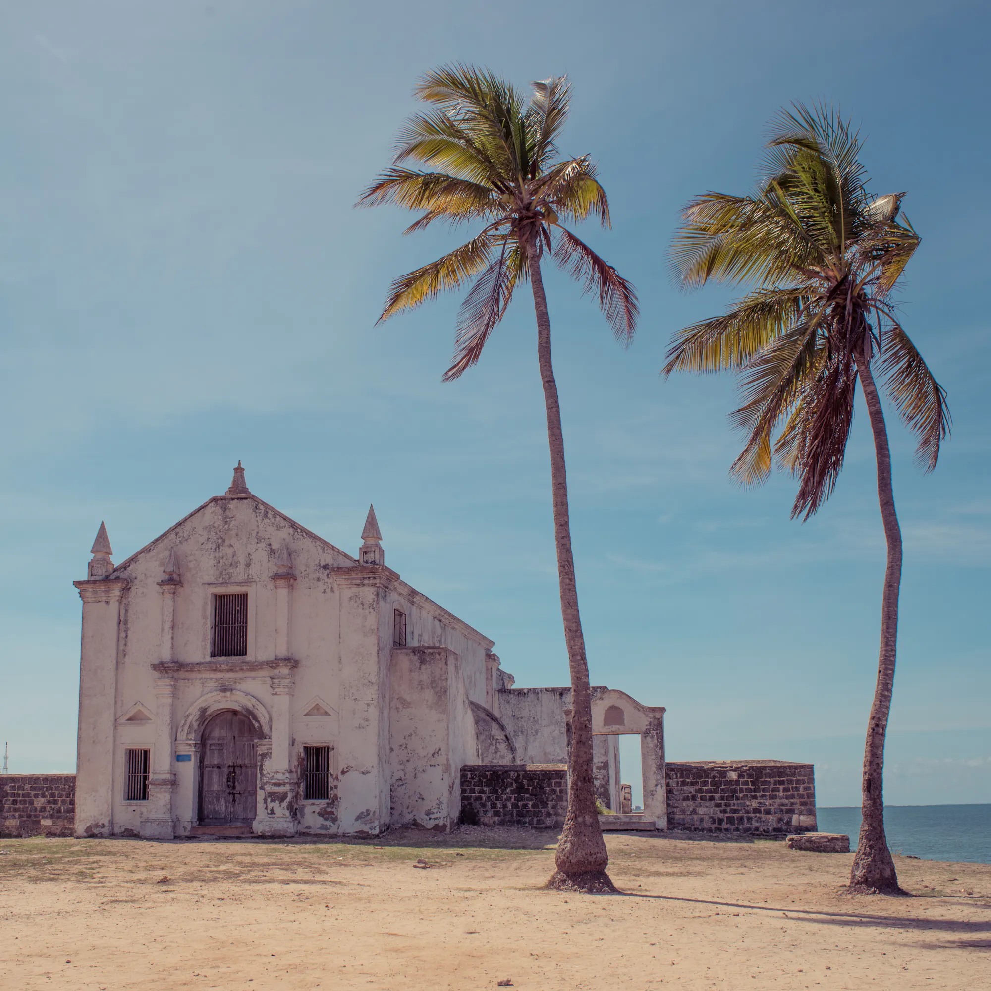 A whitewashed colonial church stands beside palm trees on the sandy shore of Ilha de Moçambique.