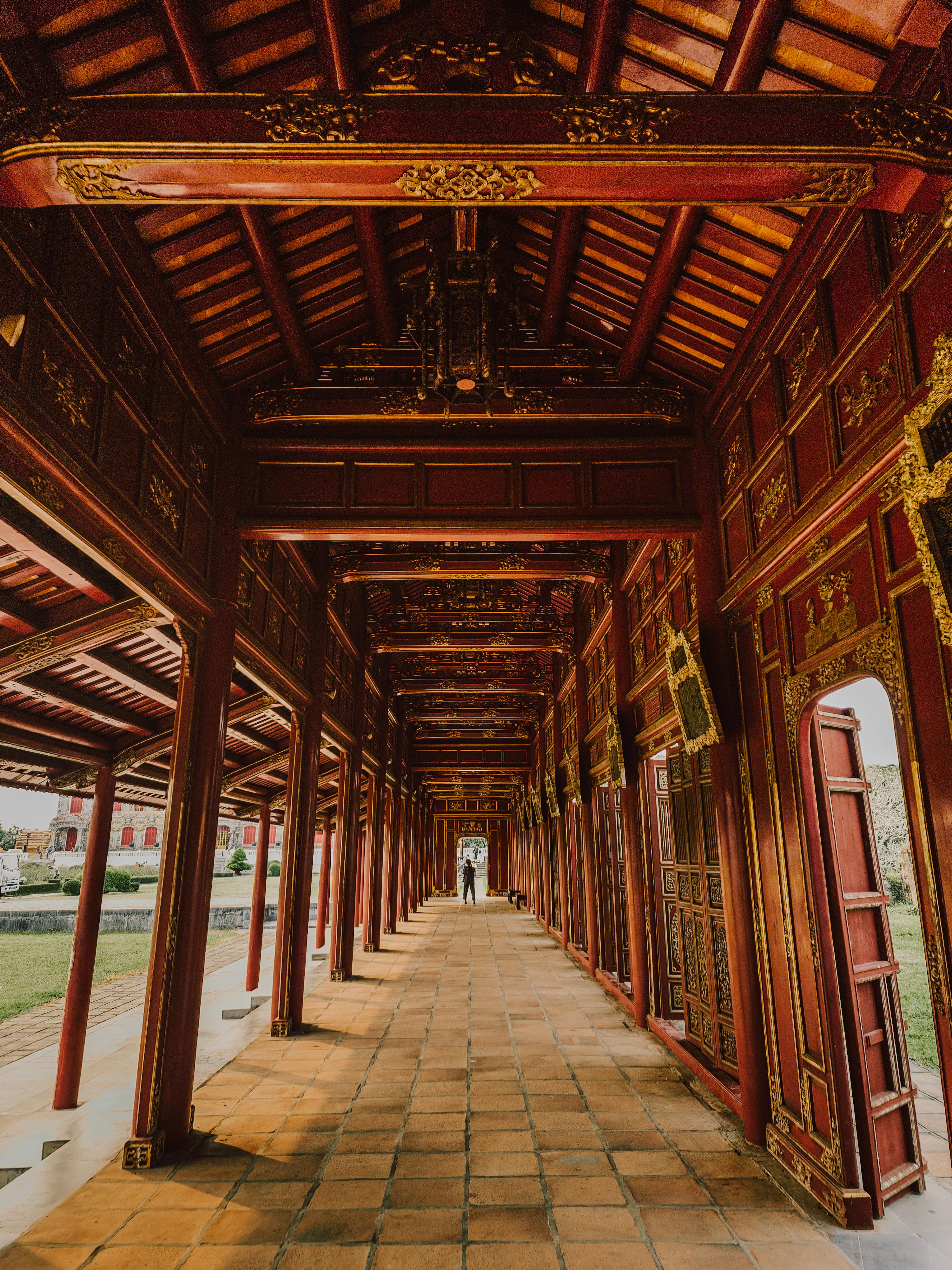 A long wooden corridor with carved pillars and tiled floor leads through a traditional Hue temple.