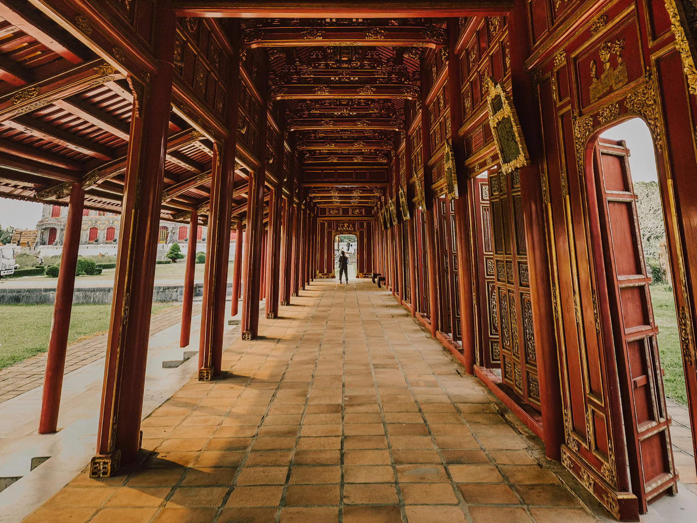 A long wooden corridor with carved pillars and tiled floor leads through a traditional Hue temple.