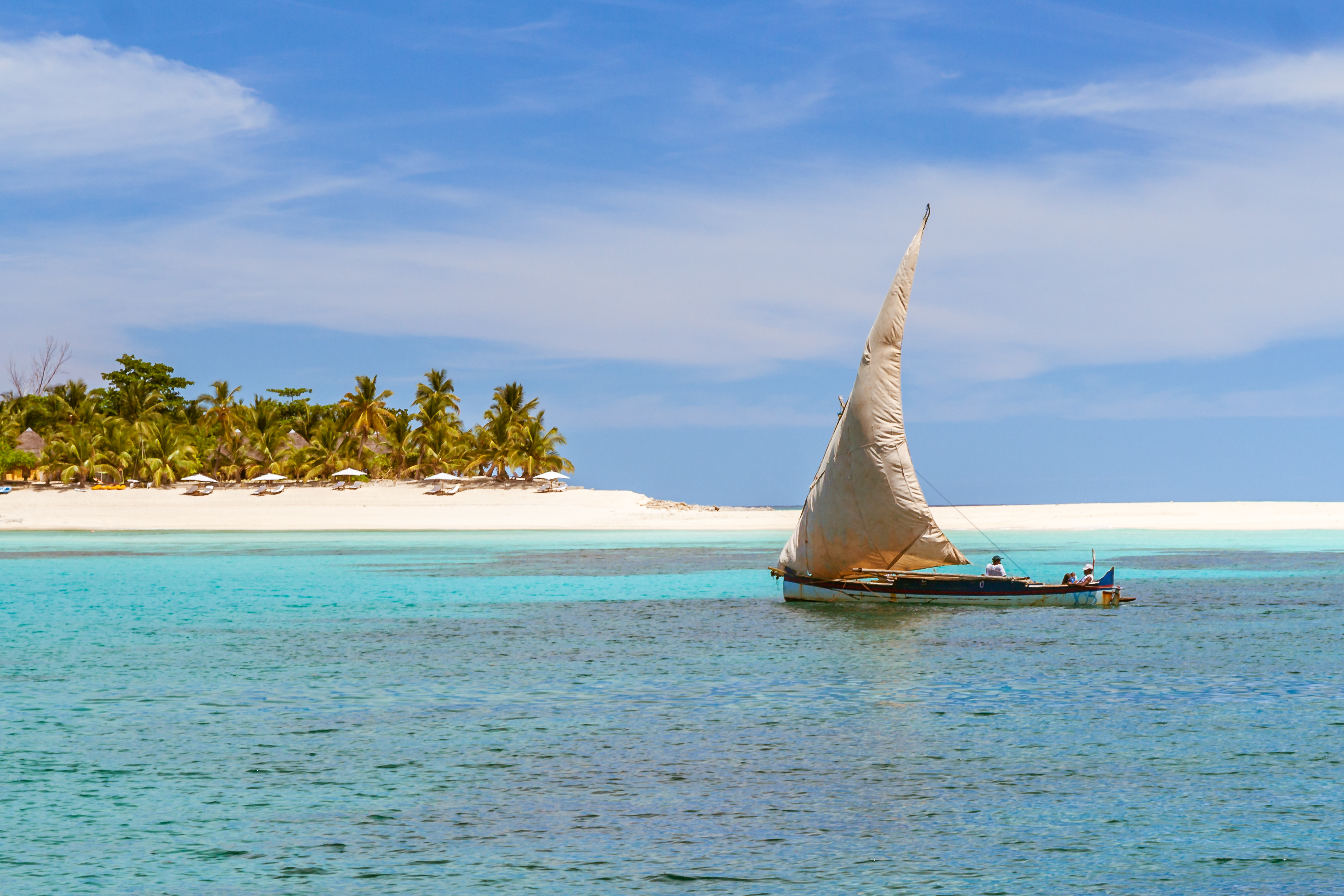 A traditional wooden sailing dhow glides past palm-fringed shores near Nosy Be, Madagascar.