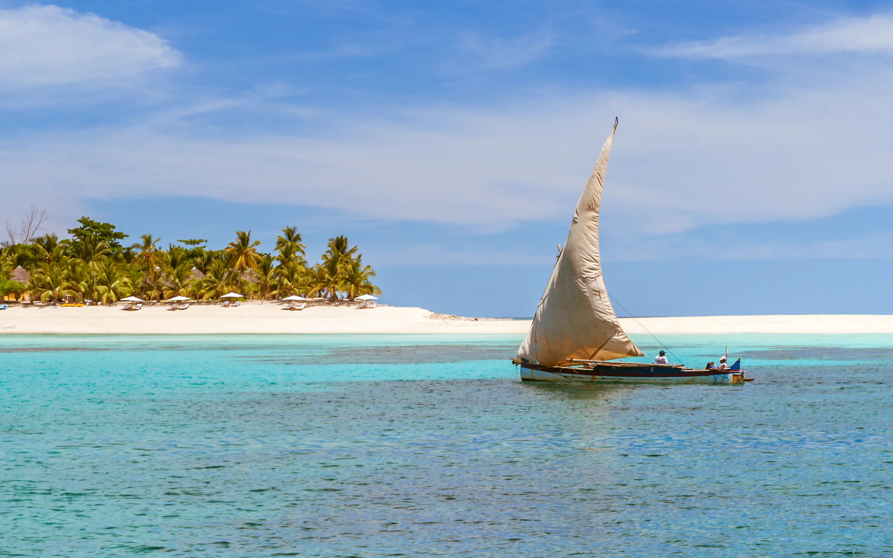 A traditional wooden sailing dhow glides past palm-fringed shores near Nosy Be, Madagascar.