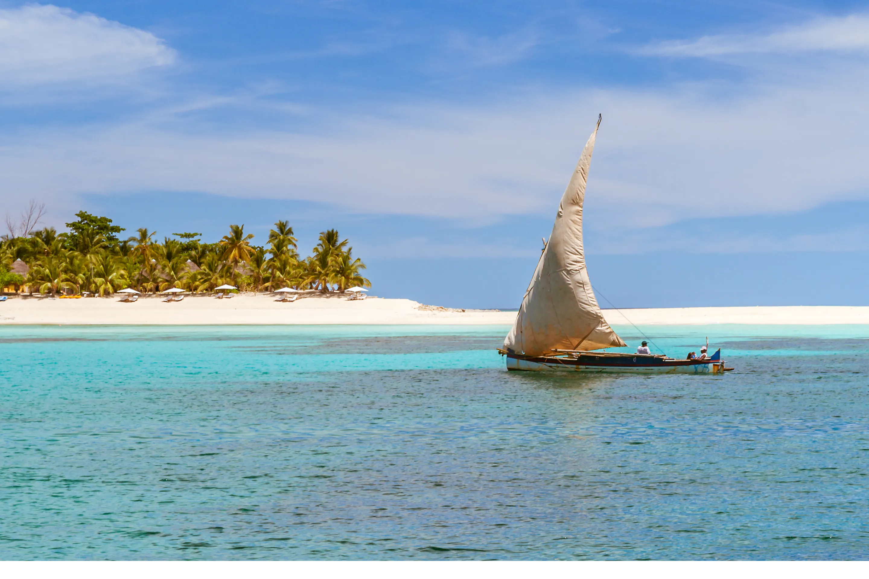 A traditional wooden sailing dhow glides past palm-fringed shores near Nosy Be, Madagascar.