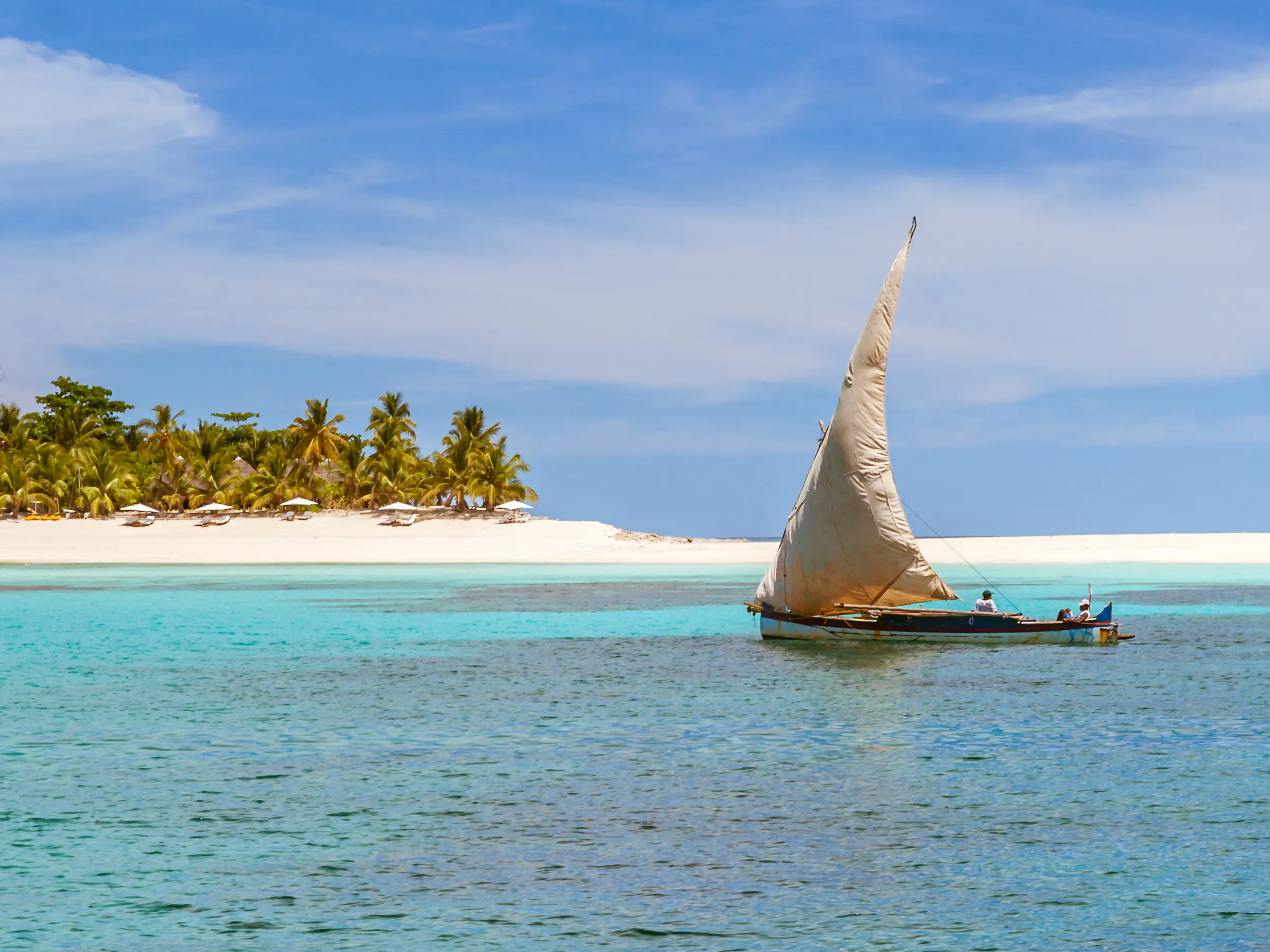 A traditional wooden sailing dhow glides past palm-fringed shores near Nosy Be, Madagascar.