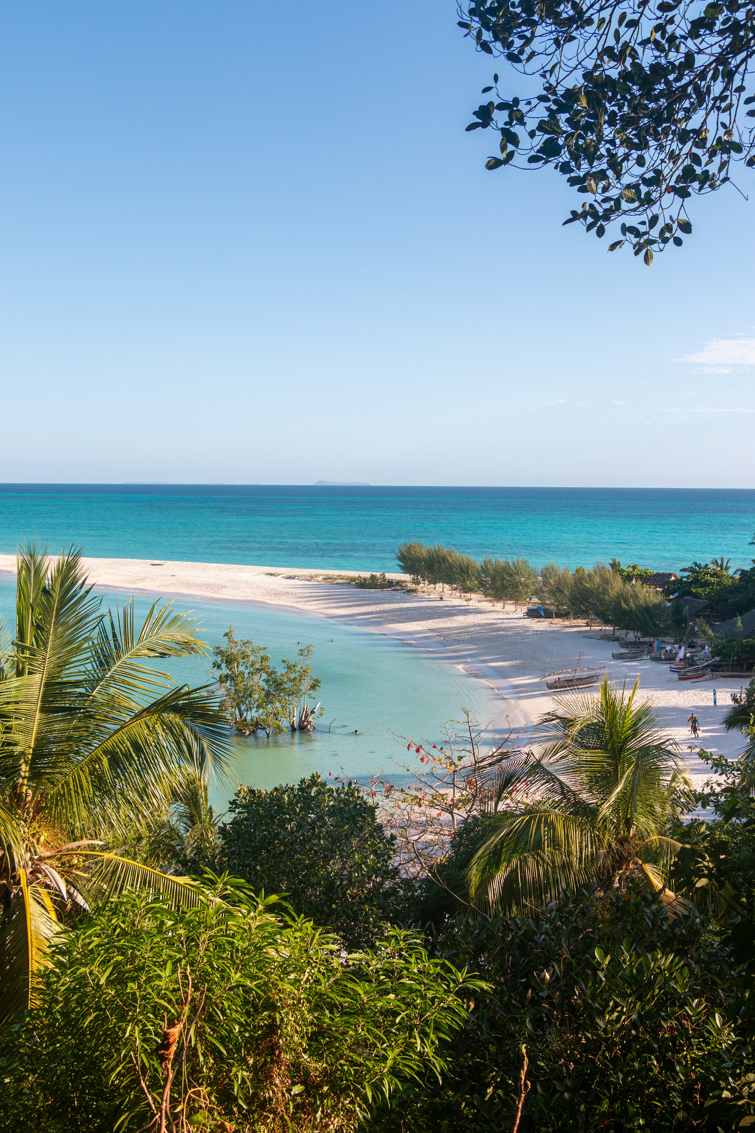 Turquoise water laps a pristine sandy beach framed by lush tropical vegetation in northern Madagascar.