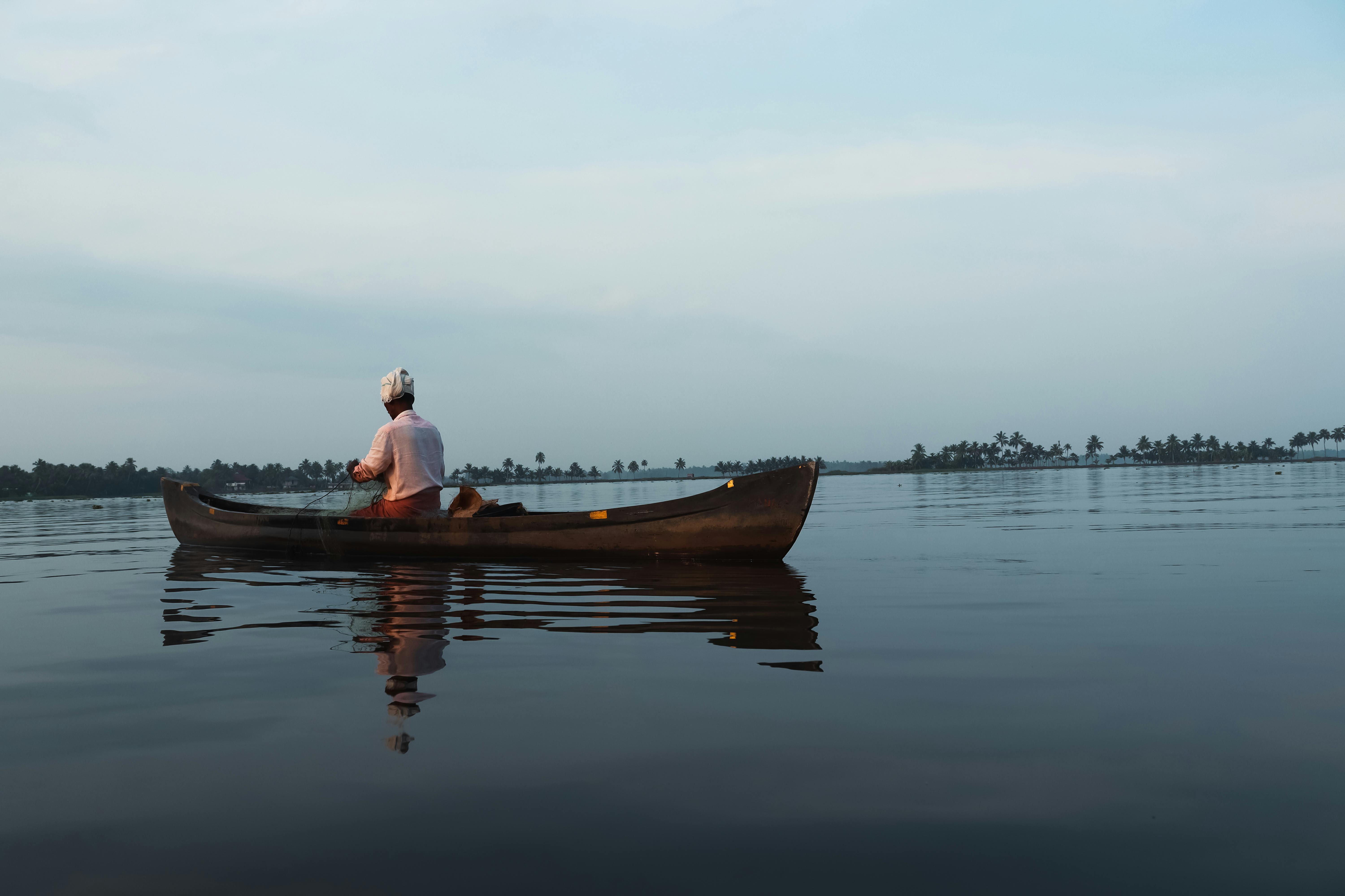 A wooden houseboat drifts slowly along a calm palm-lined backwater canal in Kerala, India.