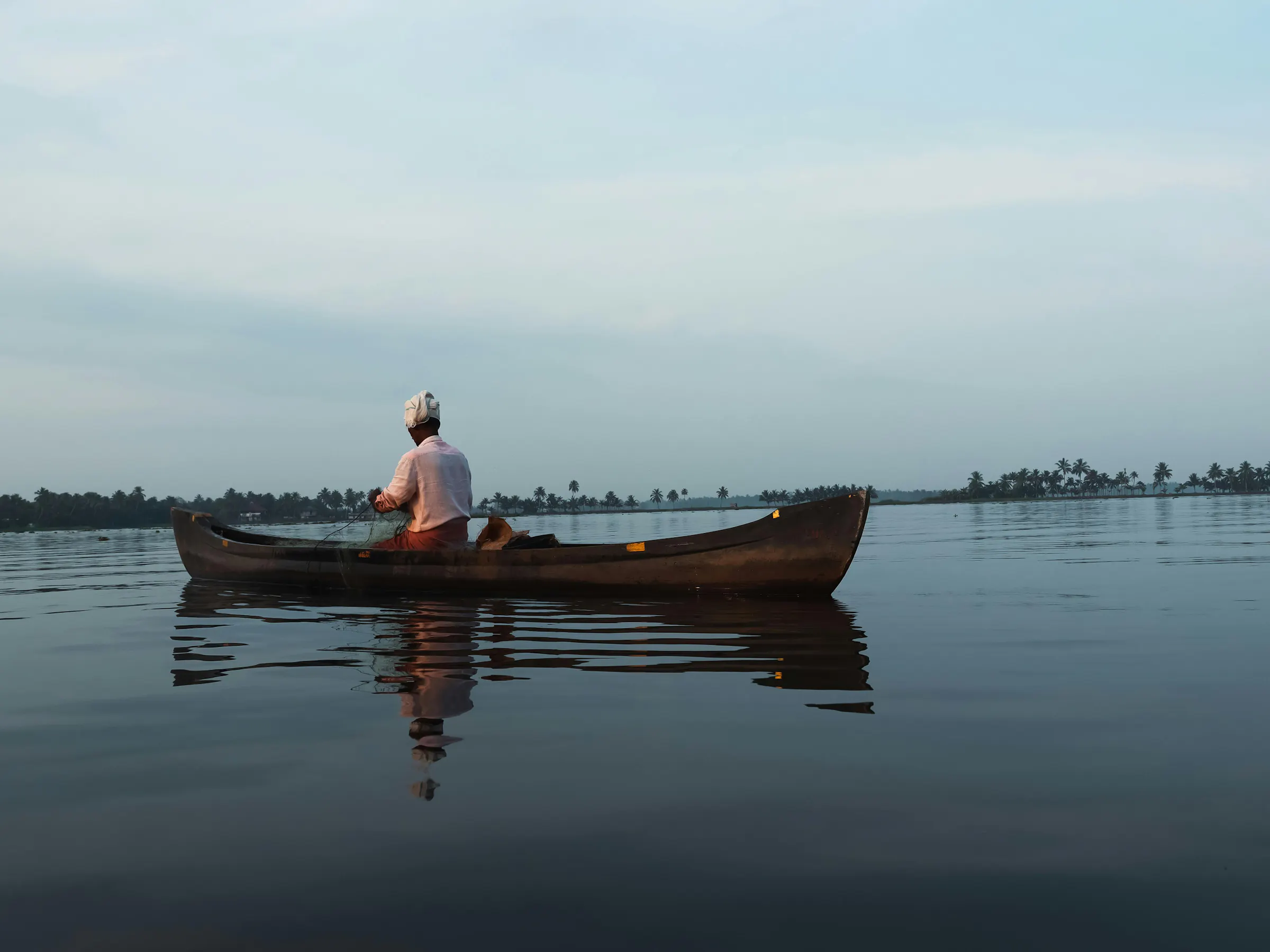 A wooden houseboat drifts slowly along a calm palm-lined backwater canal in Kerala, India.