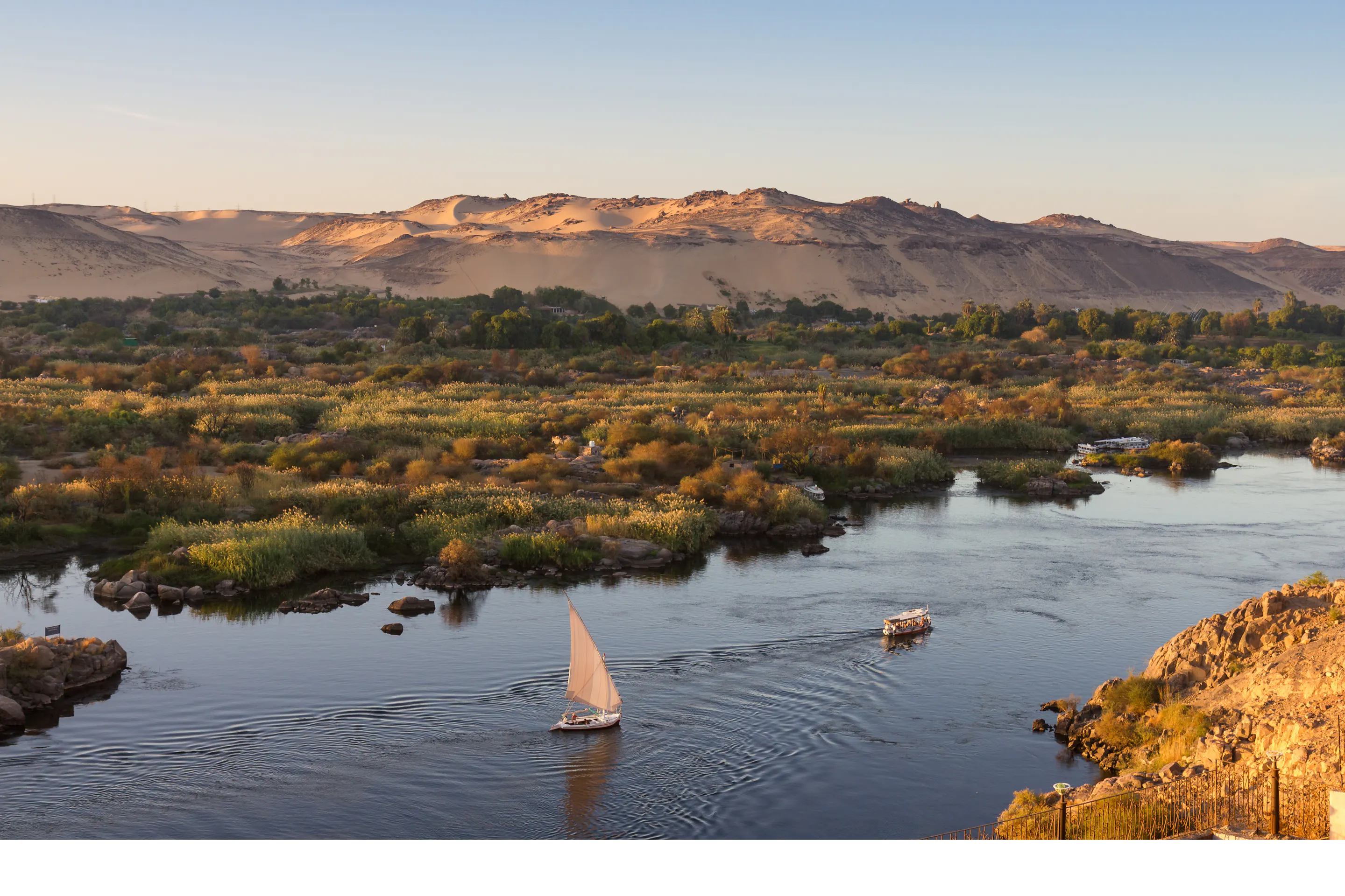 A felucca sailboat glides along the calm Nile River at Aswan with rocky banks in the background.