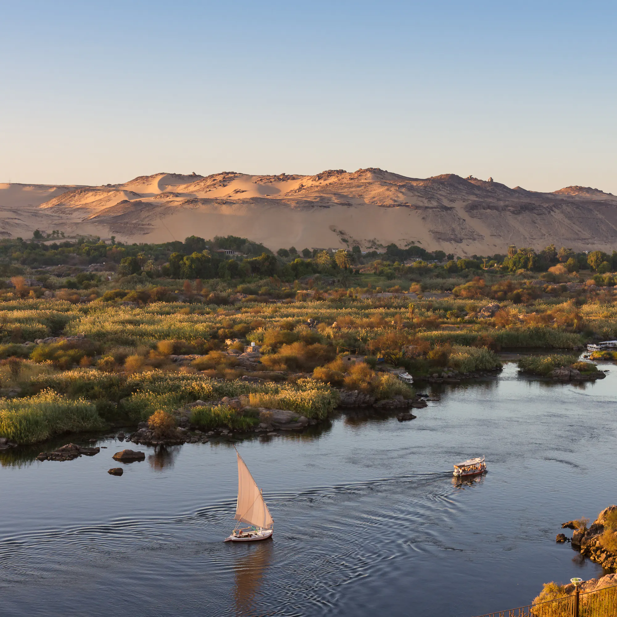 A felucca sailboat glides along the calm Nile River at Aswan with rocky banks in the background.