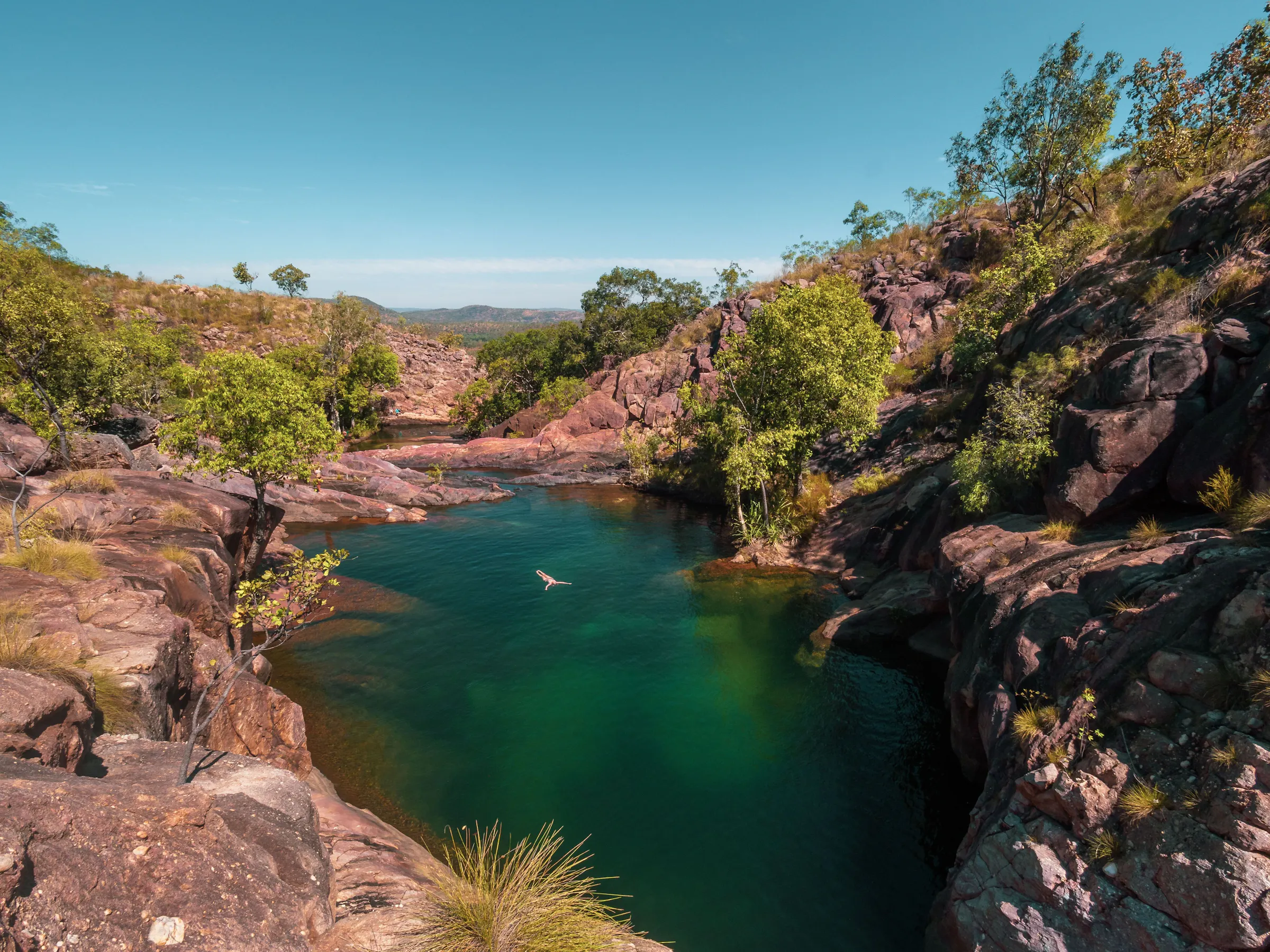 A natural rock infinity pool at Gunlom overlooks a sweeping green valley in Australia's Northern Territory.