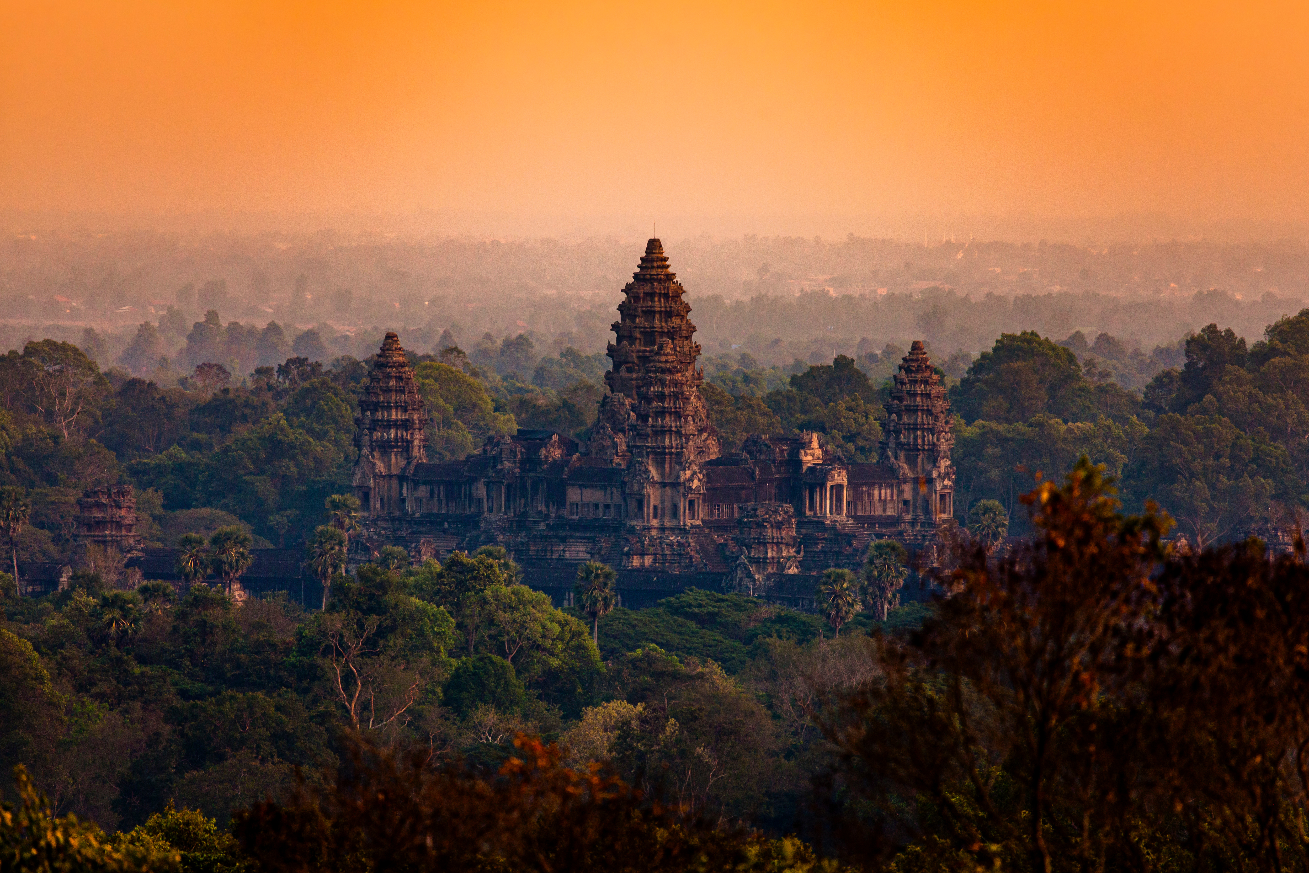 The temple towers of Angkor Wat are reflected in a still pool at dusk under a deep orange sky.
