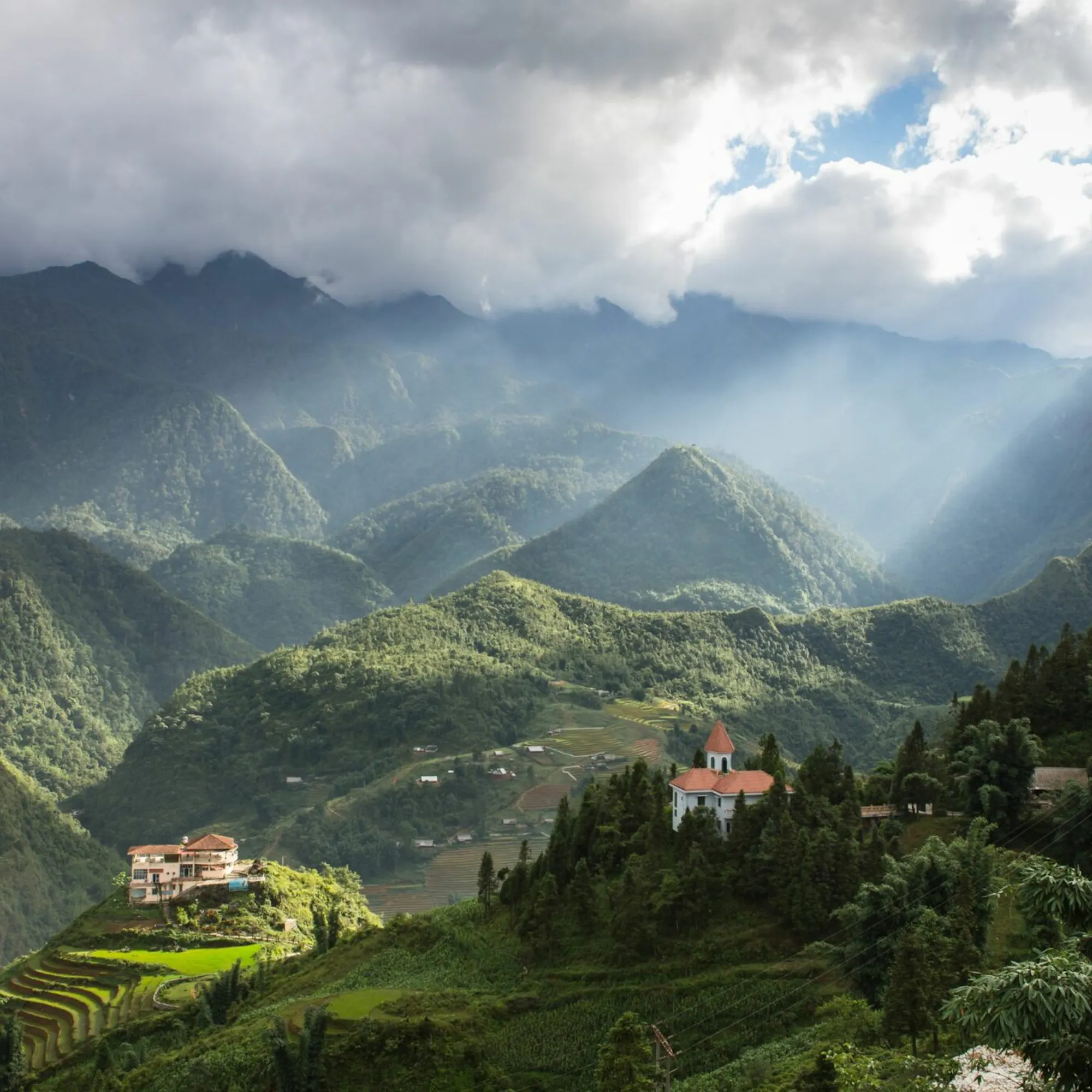 Mist-shrouded mountains rise behind a forested valley and distant terraced hillsides in Sapa.