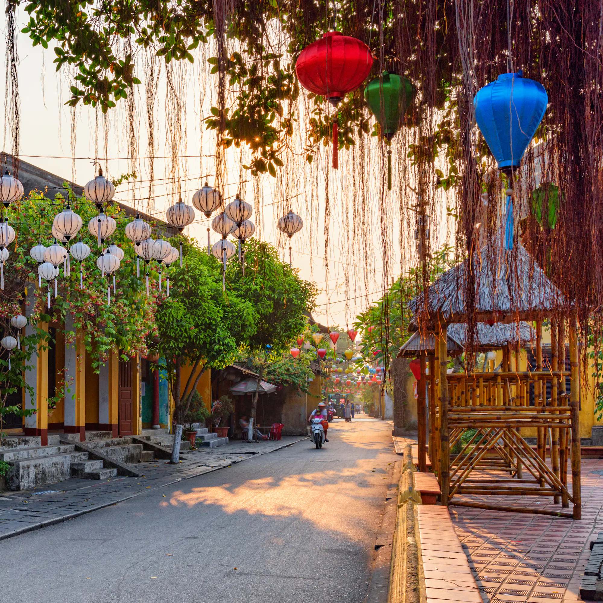 Silk lanterns in vivid red, yellow, and blue hang above a golden-walled street in Hoi An at dusk.