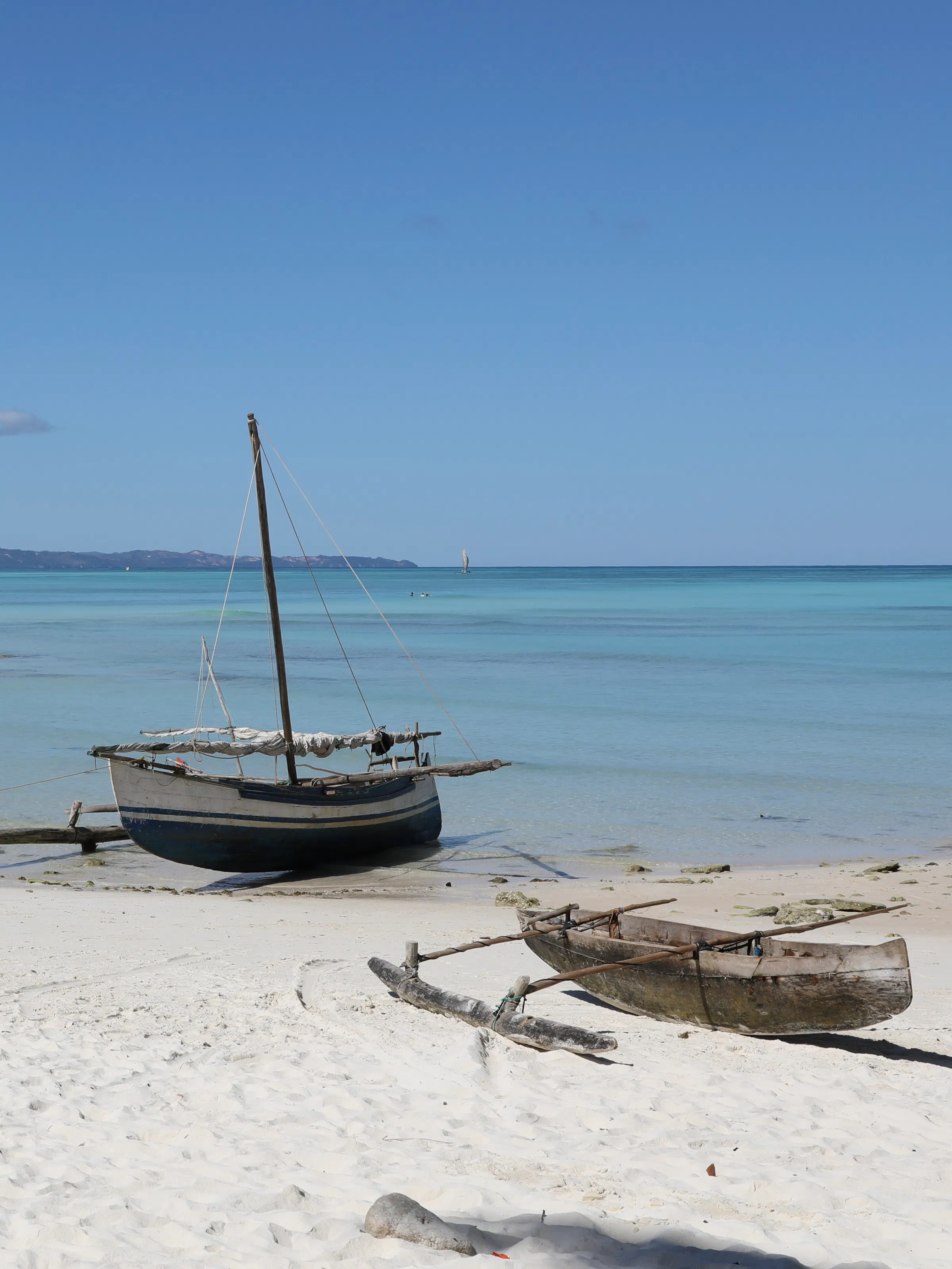 A traditional wooden outrigger canoe floats in calm turquoise water near Nosy Iranja, Mozambique.