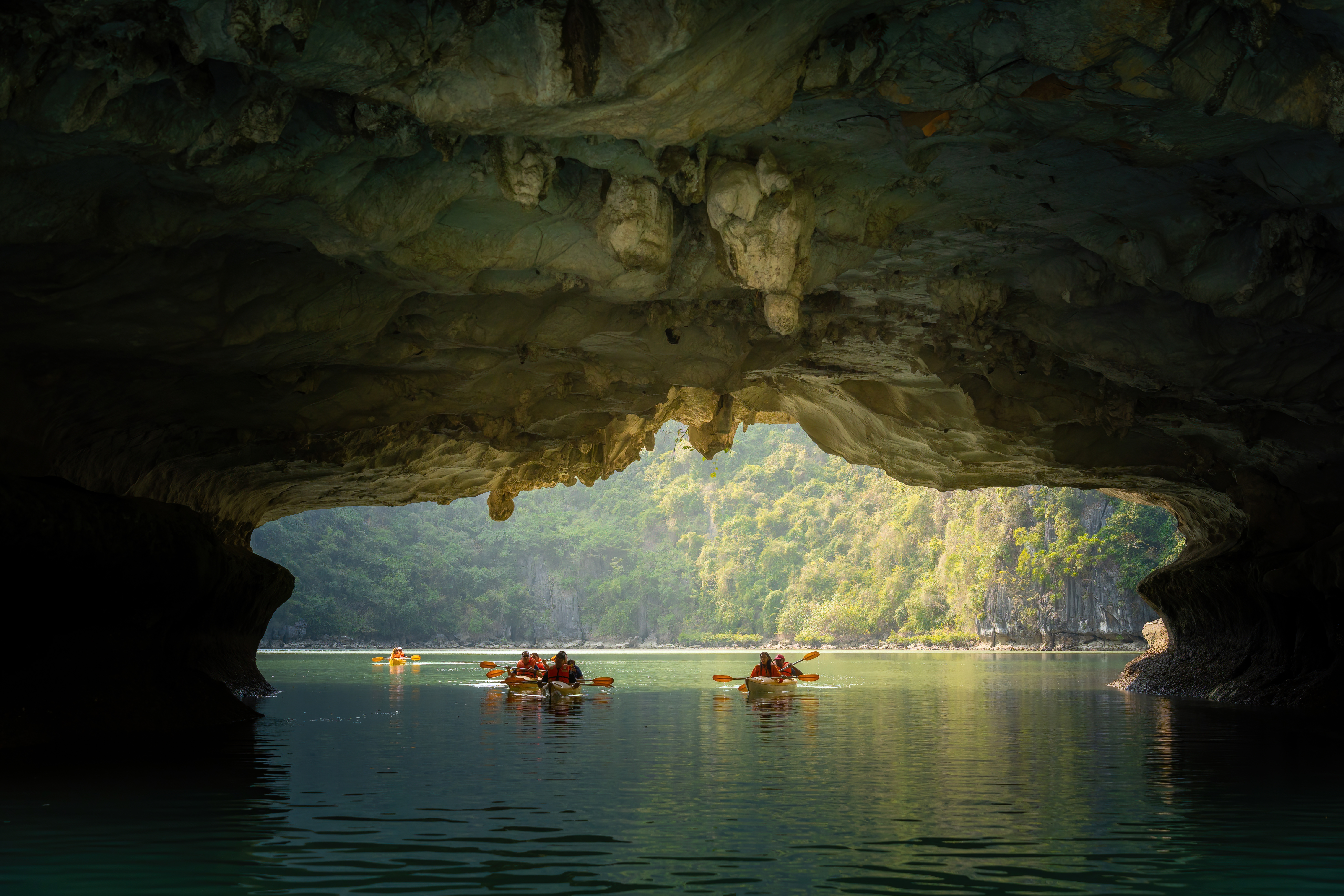 A kayaker paddles through calm jade-green waters between towering limestone karsts in Ha Long Bay.