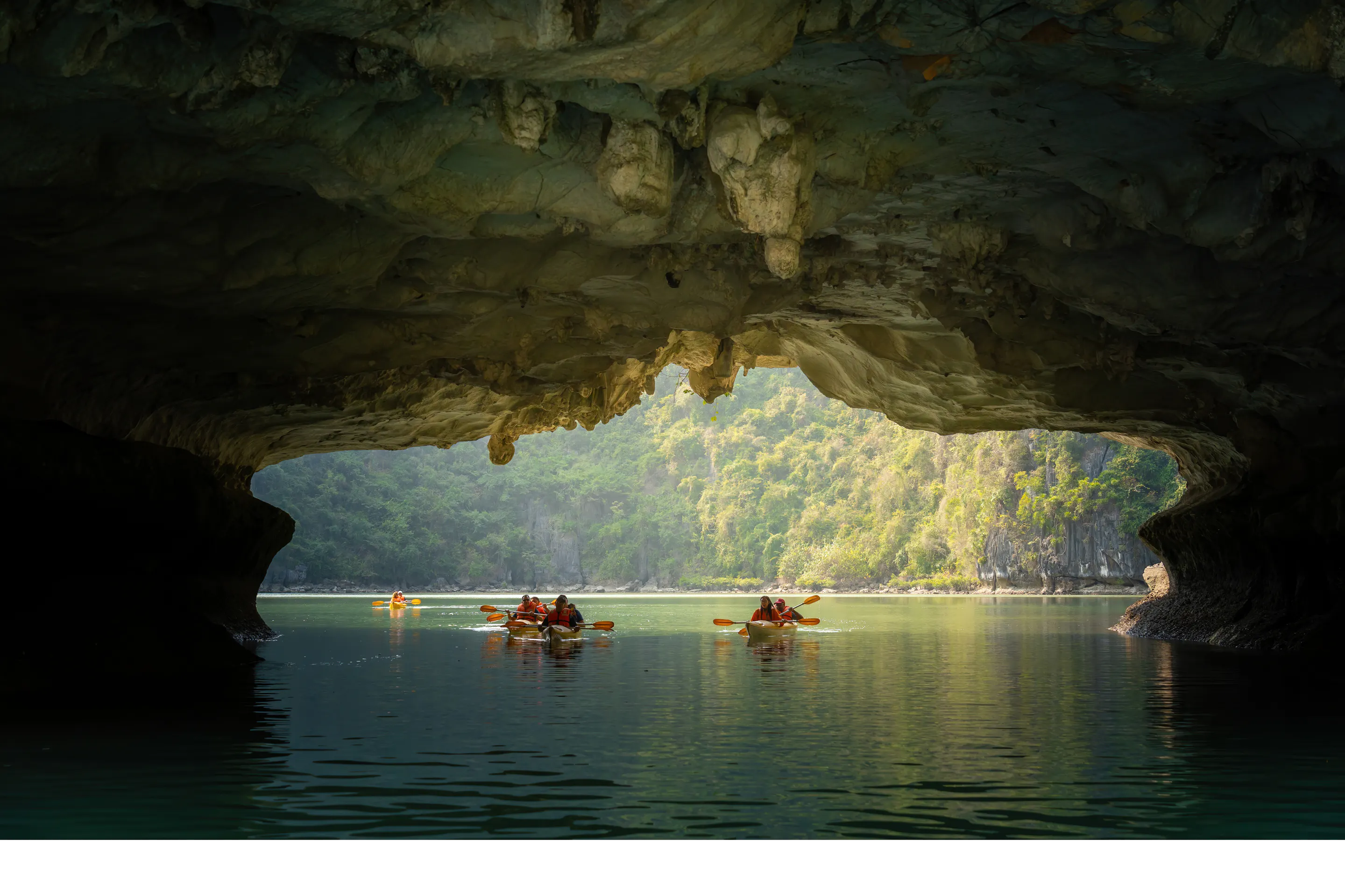 A kayaker paddles through calm jade-green waters between towering limestone karsts in Ha Long Bay.