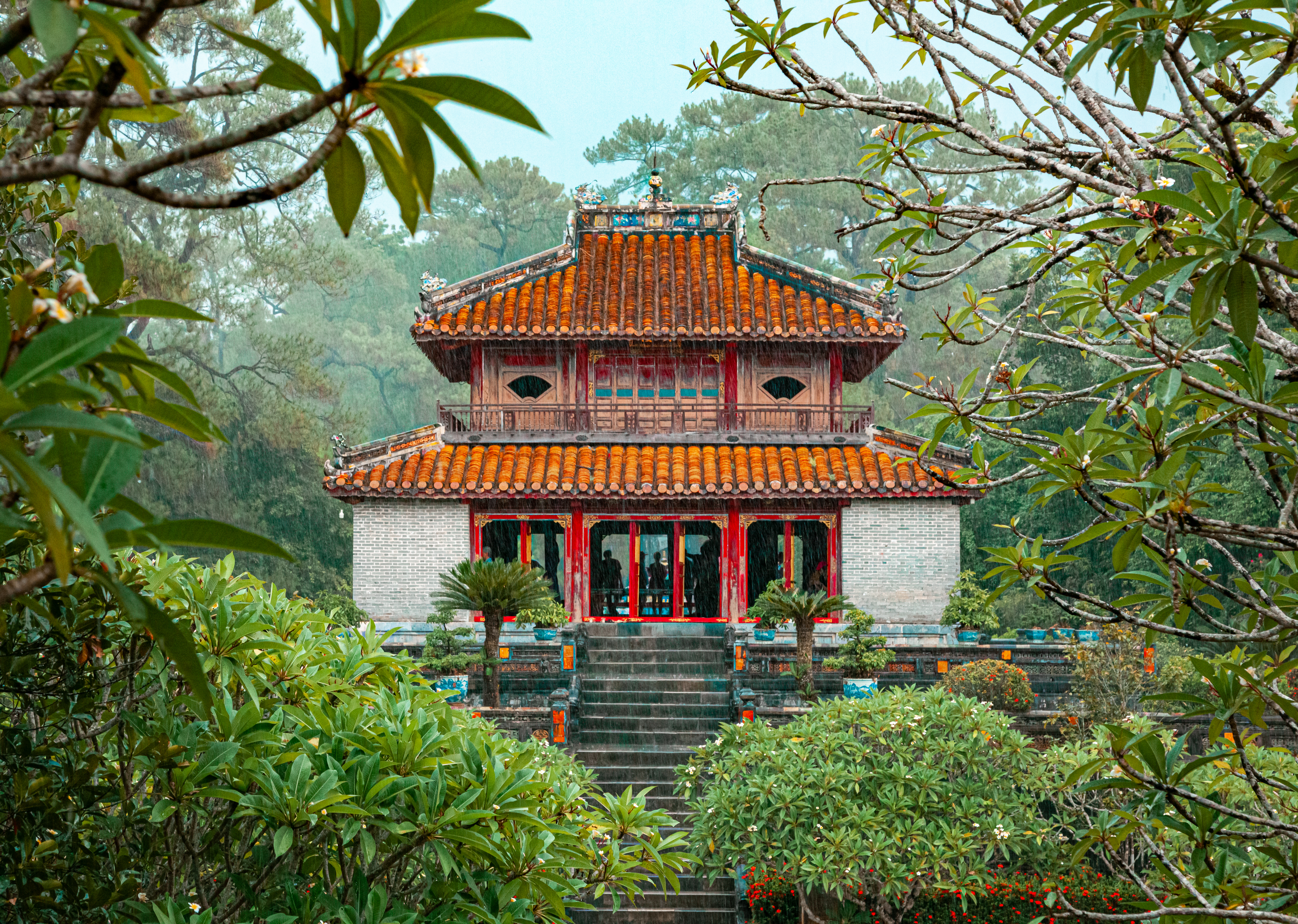 The ornate red and gold Minh Mang Temple is framed by tropical trees and a garden in Hue.