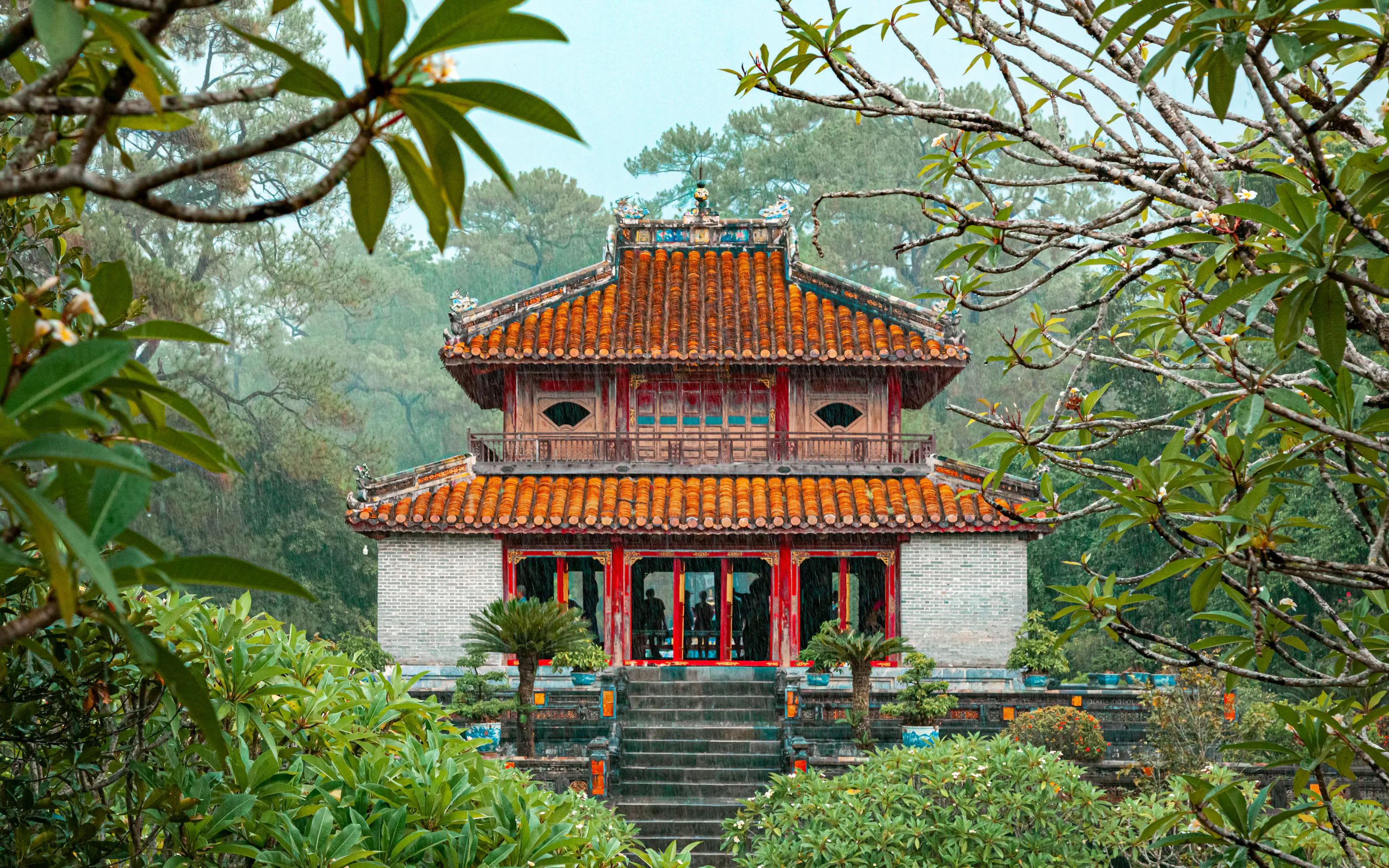 The ornate red and gold Minh Mang Temple is framed by tropical trees and a garden in Hue.