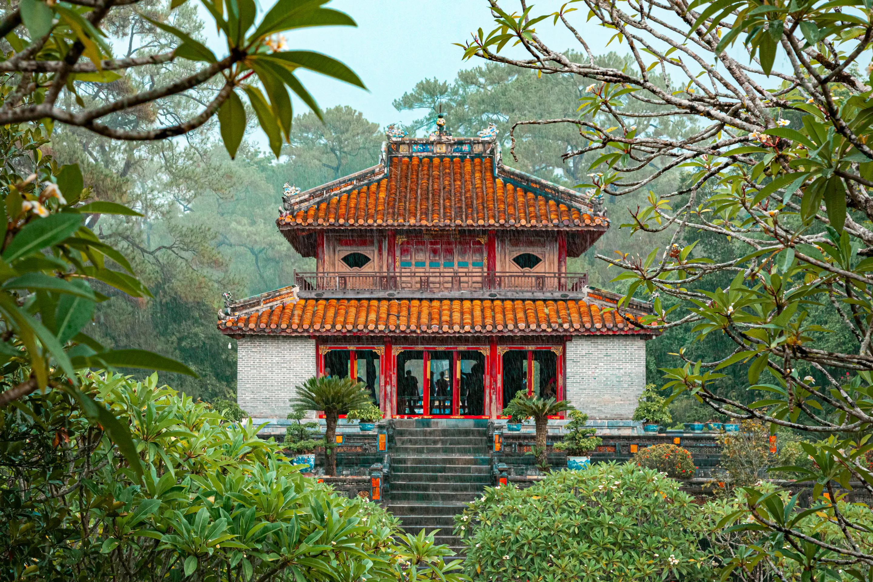 The ornate red and gold Minh Mang Temple is framed by tropical trees and a garden in Hue.