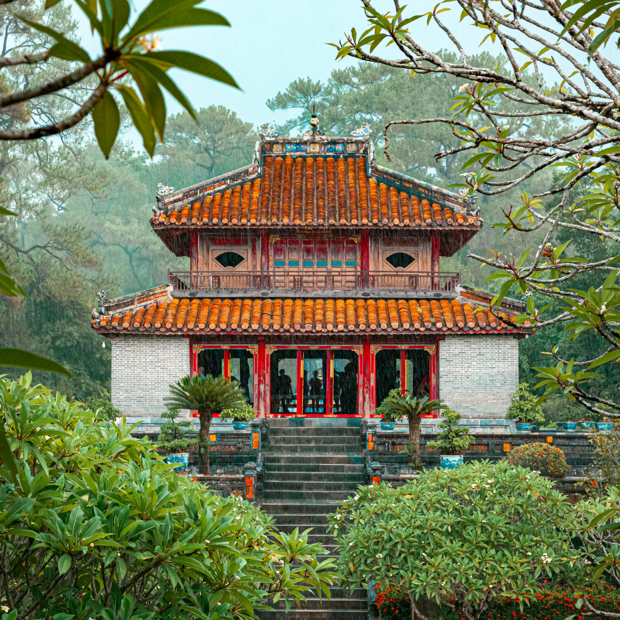 The ornate red and gold Minh Mang Temple is framed by tropical trees and a garden in Hue.