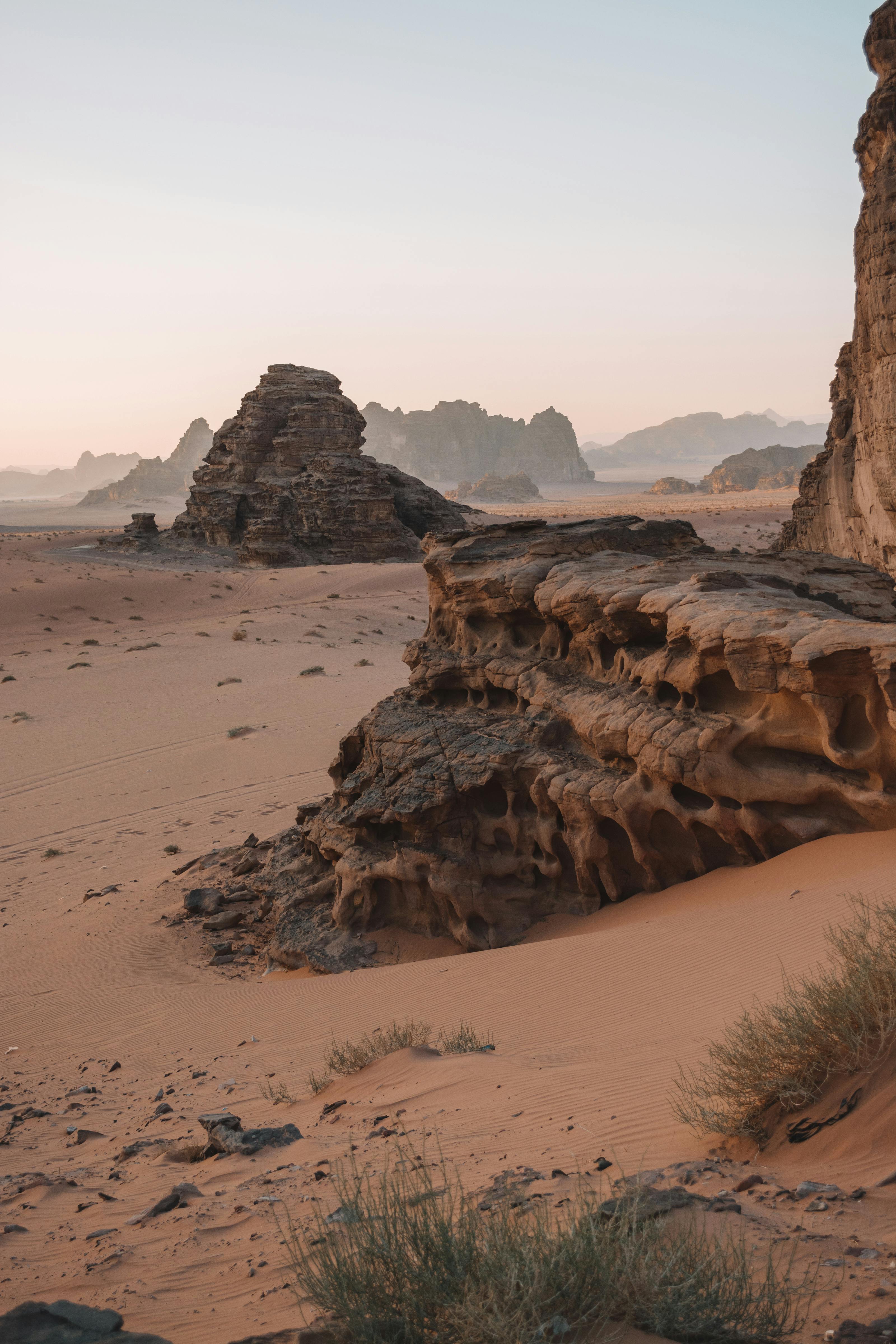Two weathered rock formations rise from the flat sandy floor of Wadi Rum under a hazy sky.