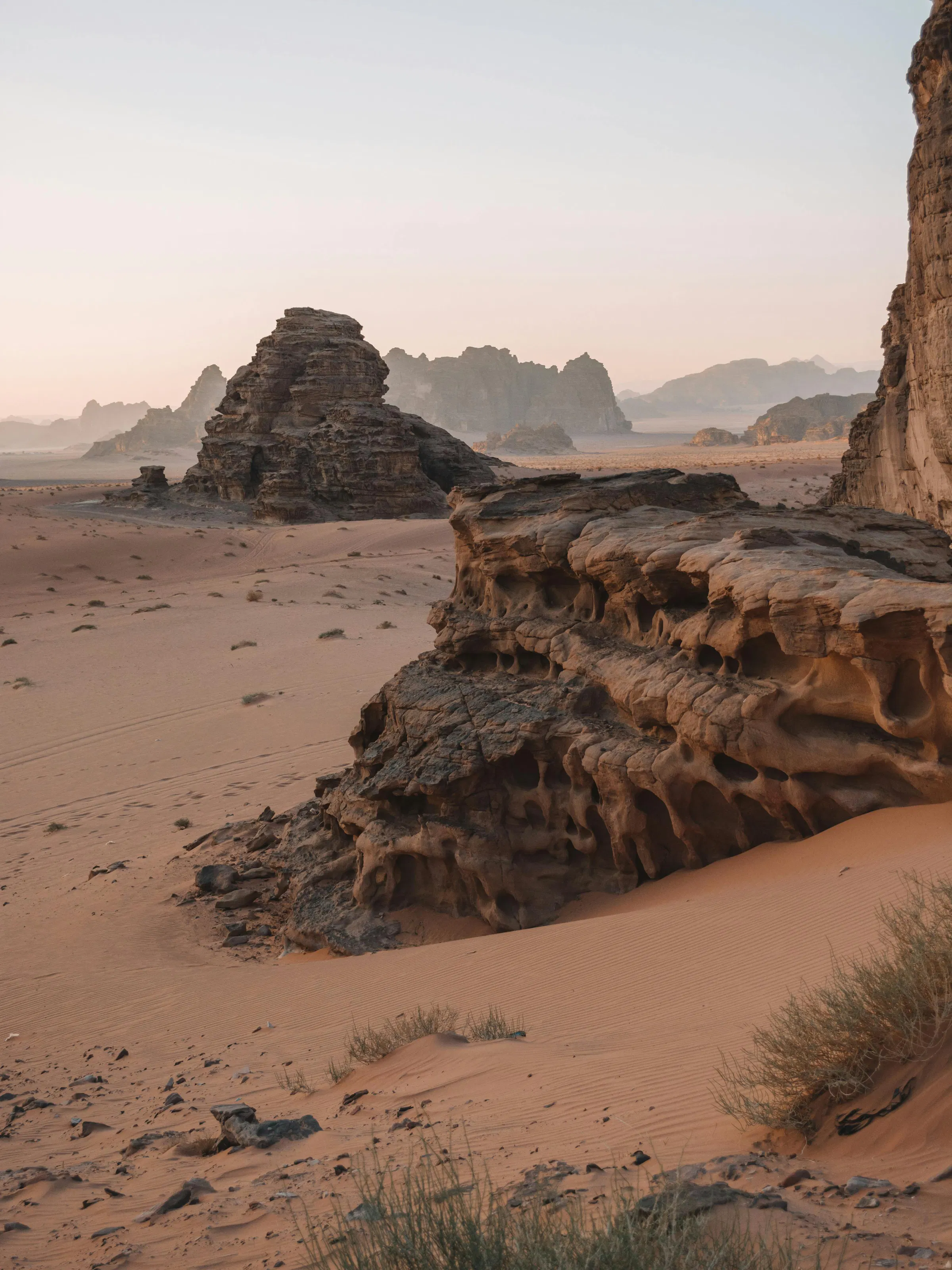 Two weathered rock formations rise from the flat sandy floor of Wadi Rum under a hazy sky.