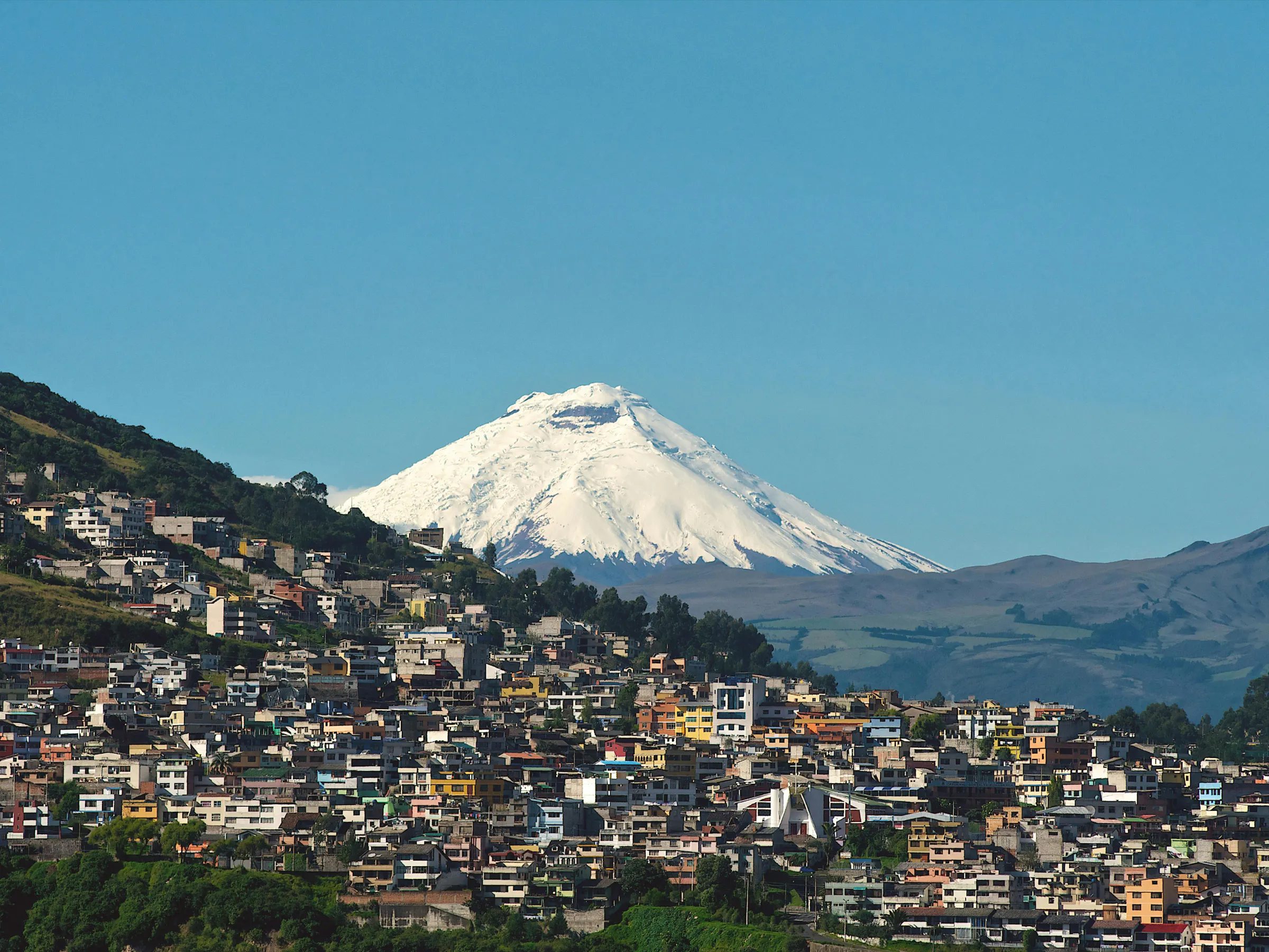 Quito's densely built cityscape fills a mountain valley with volcanic peaks visible on the horizon.